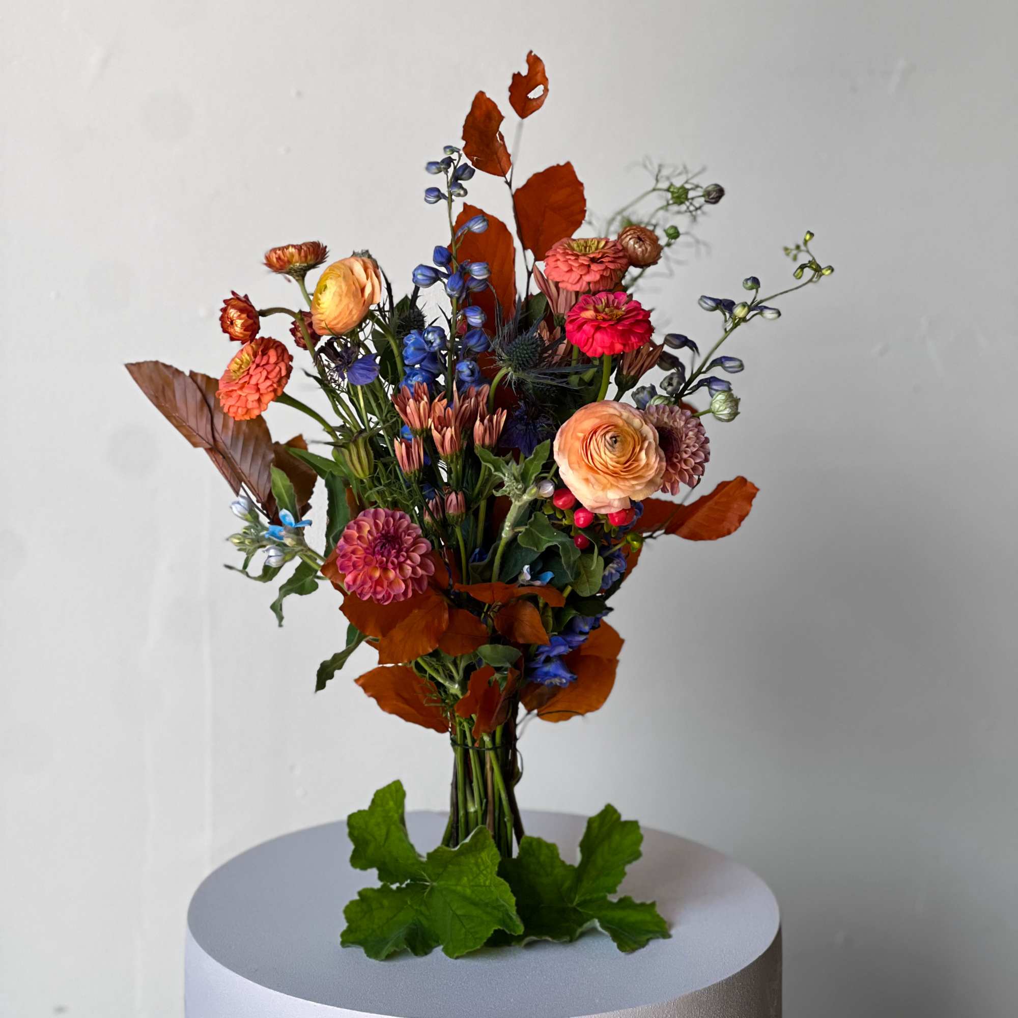 Mixed bouquet of orange, pink, and blue flowers in a clear vase