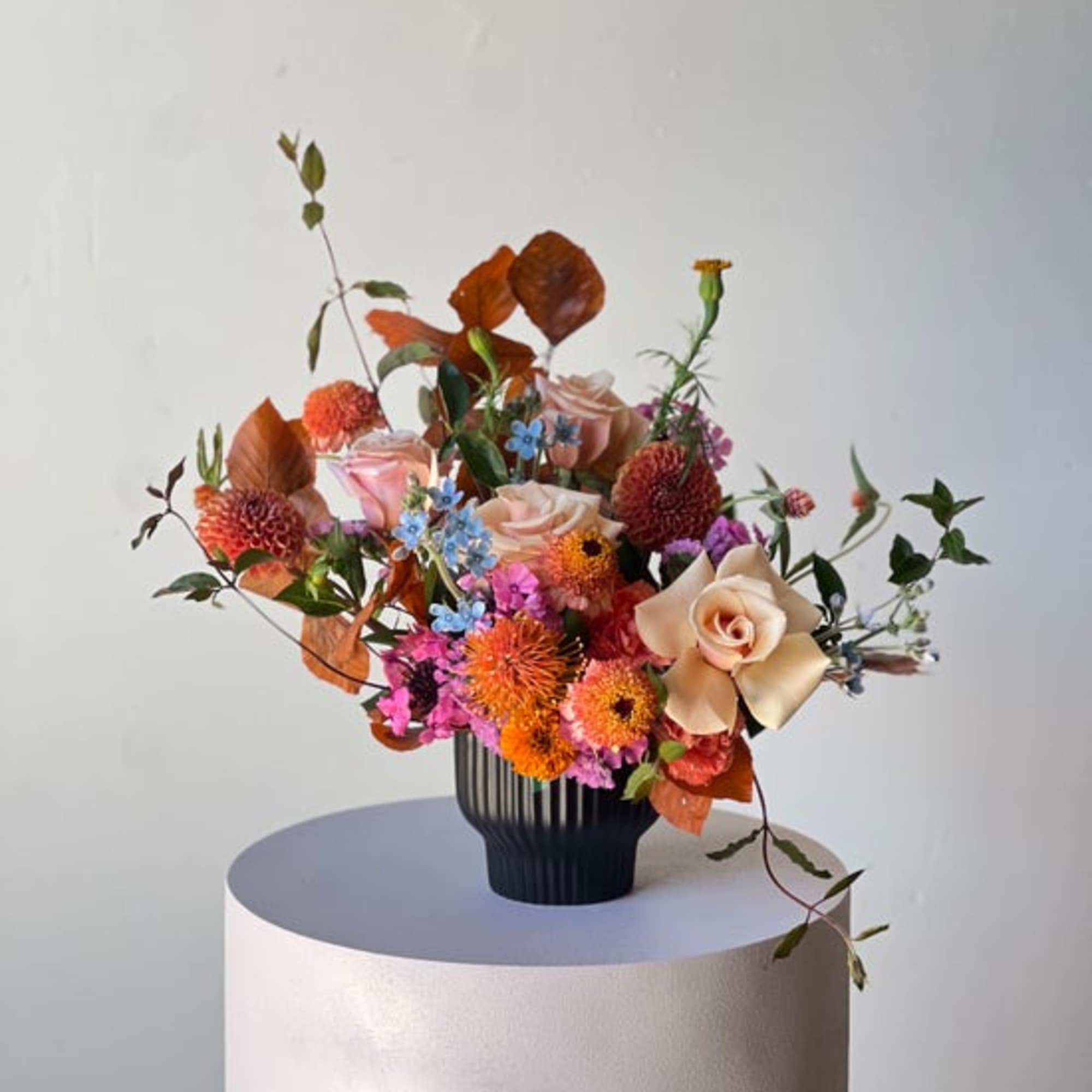 Mixed bouquet of orange, pink, and cream flowers in a black vase
