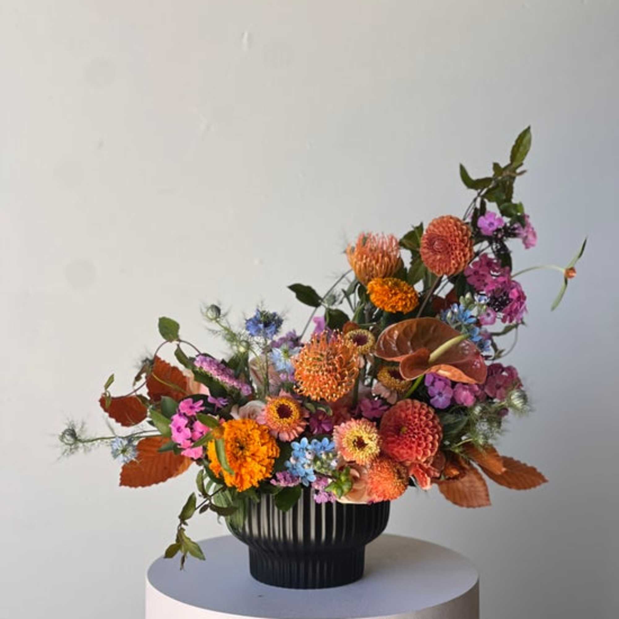 Colorful mixed flower arrangement in a black vase on a pedestal