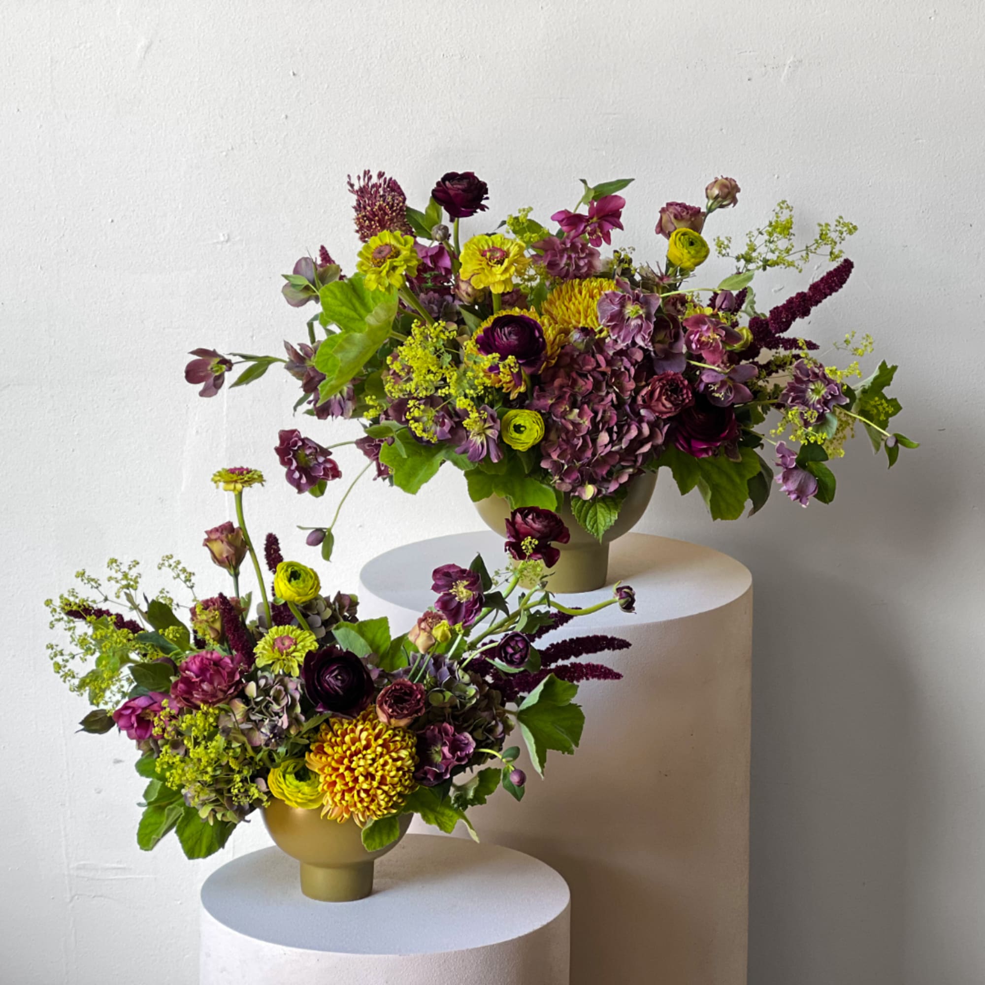 Two purple and yellow floral arrangements in gold vases on white pedestals