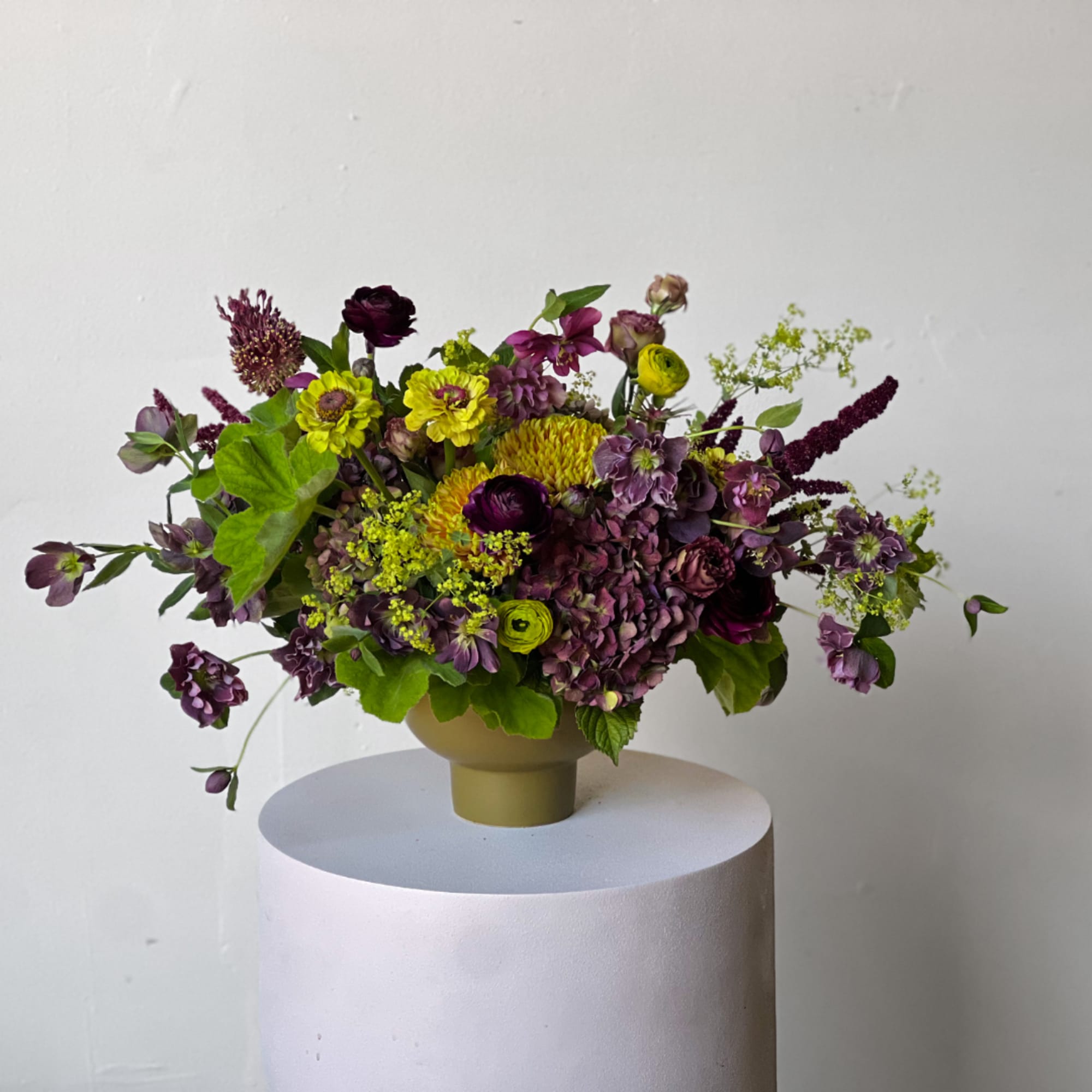 Mixed purple and yellow flower arrangement in a beige vase