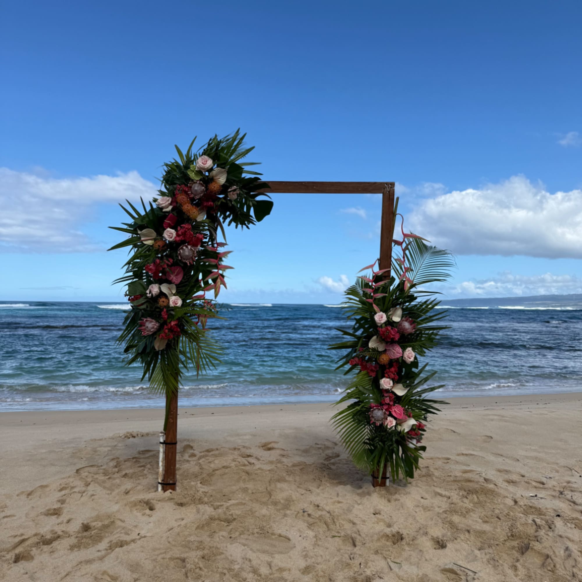 Beach wedding arch decorated with tropical flowers and palm leaves