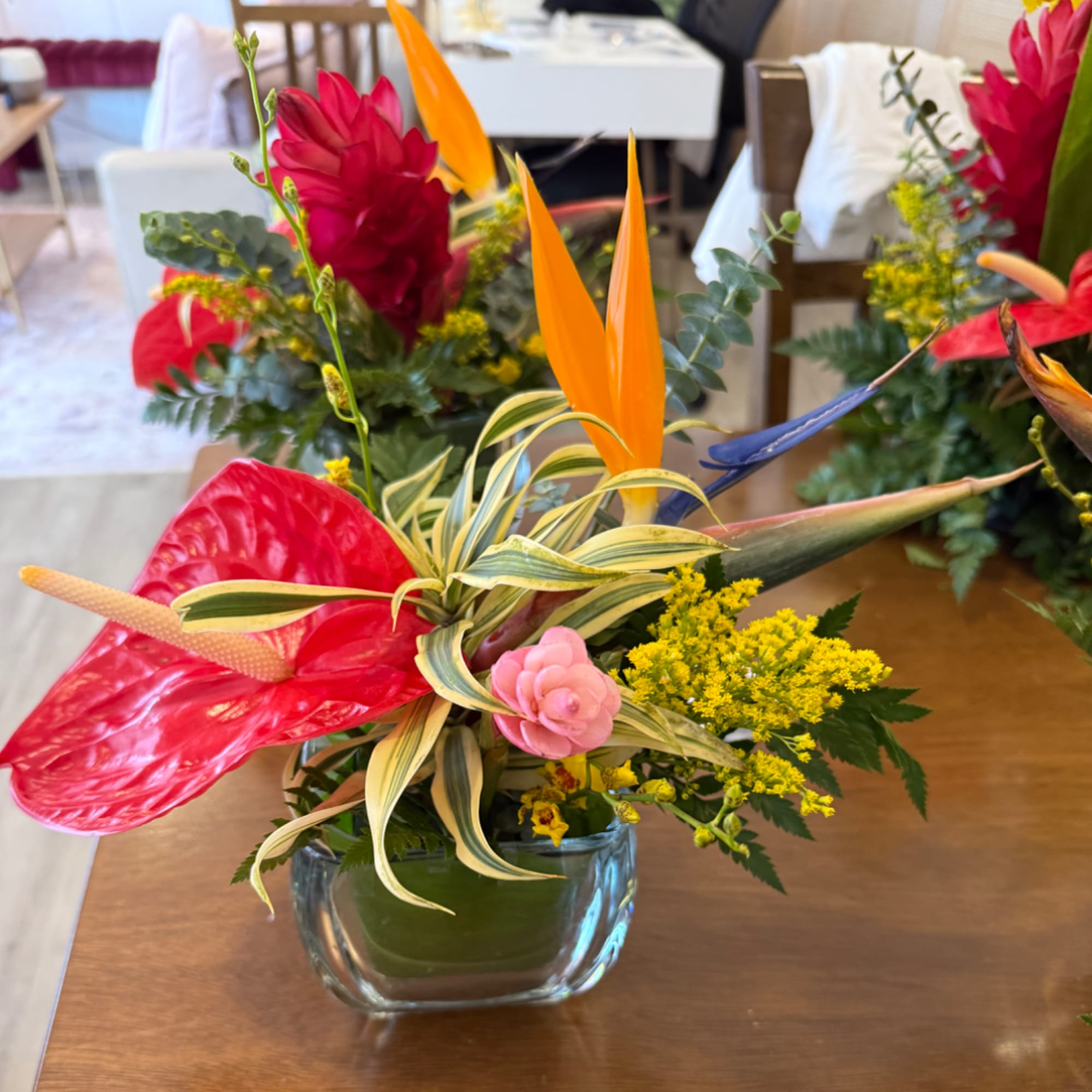 Tropical floral arrangement in a glass vase with red anthurium and orange bird of paradise.