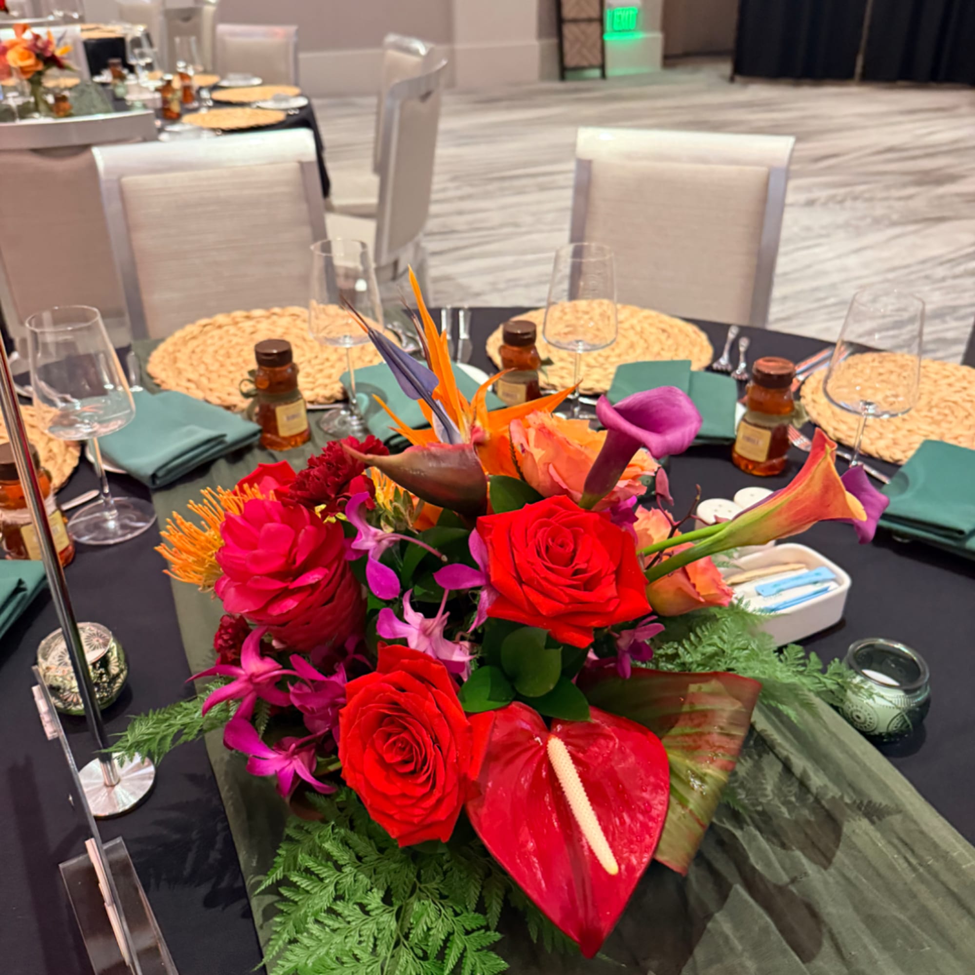 Bright tropical centerpiece with red roses, calla lilies, and anthurium on a banquet table