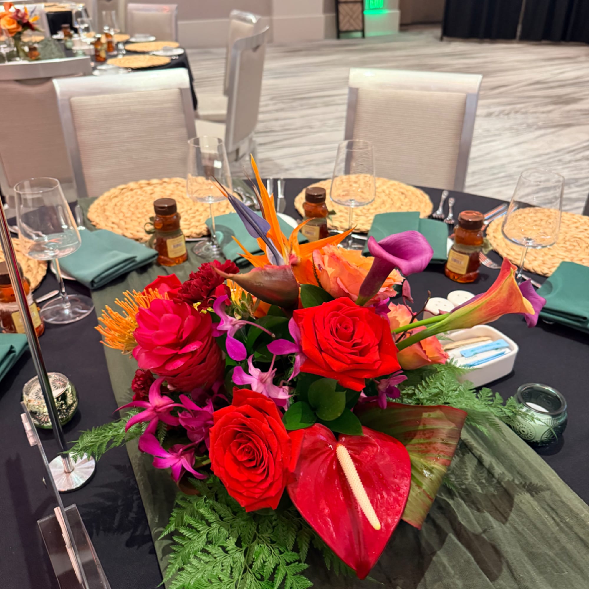 Bright tropical centerpiece with red roses, purple calla lilies, and orange bird-of-paradise
