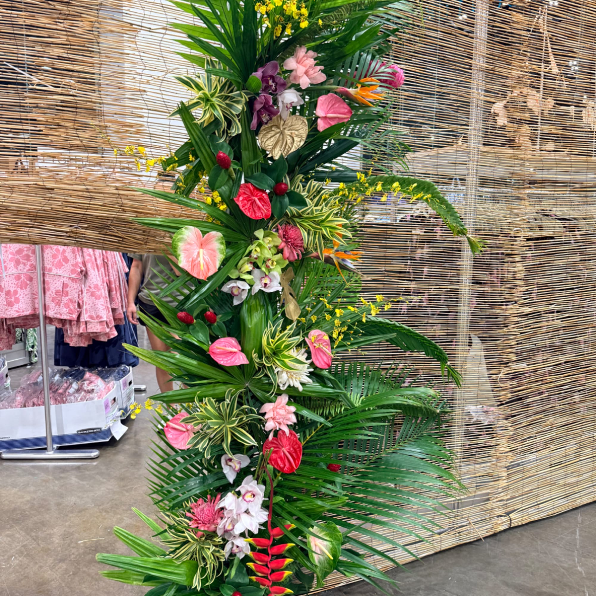 Tall tropical floral arrangement with pink and red blooms and large palm leaves