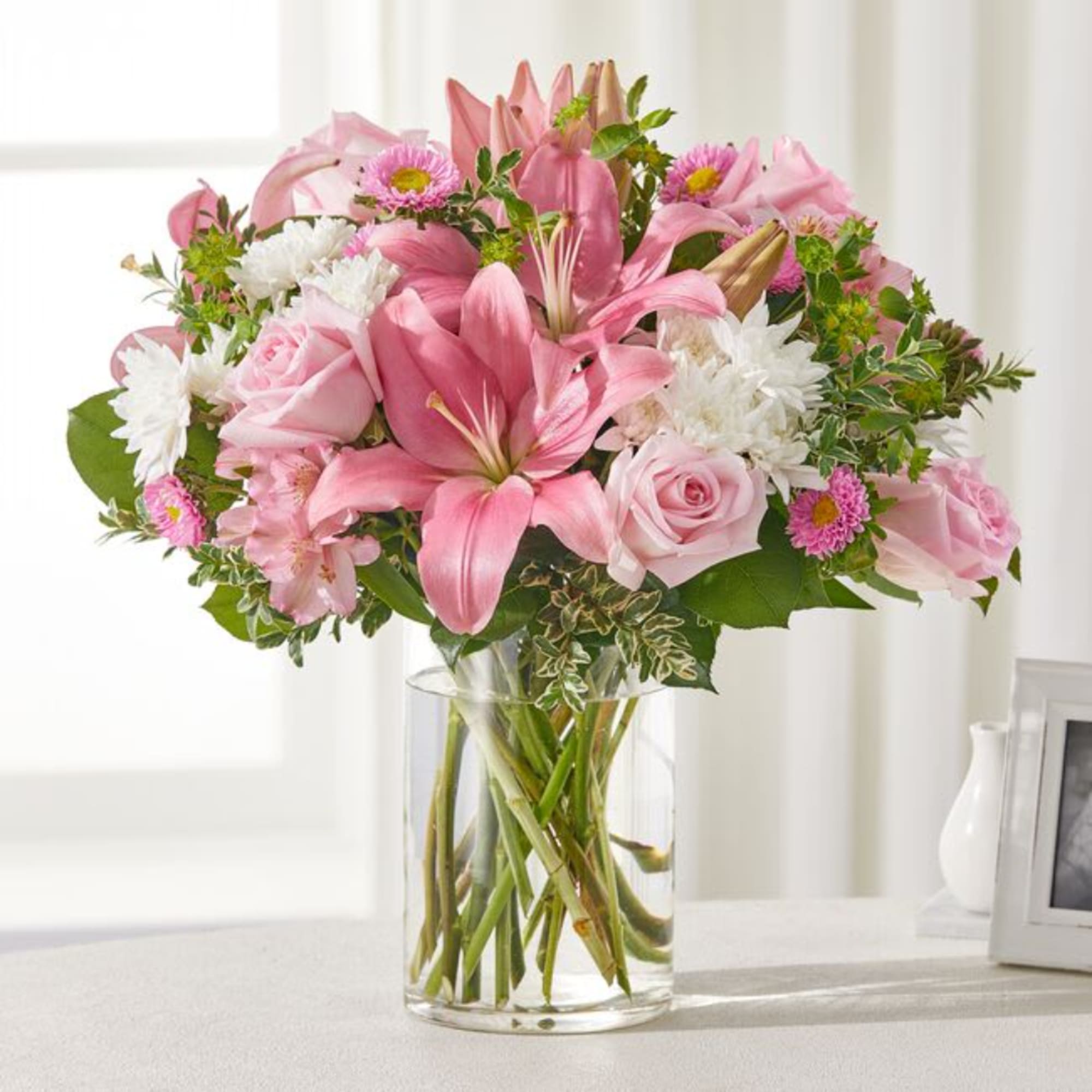 Pink lilies and roses arranged in a clear glass vase