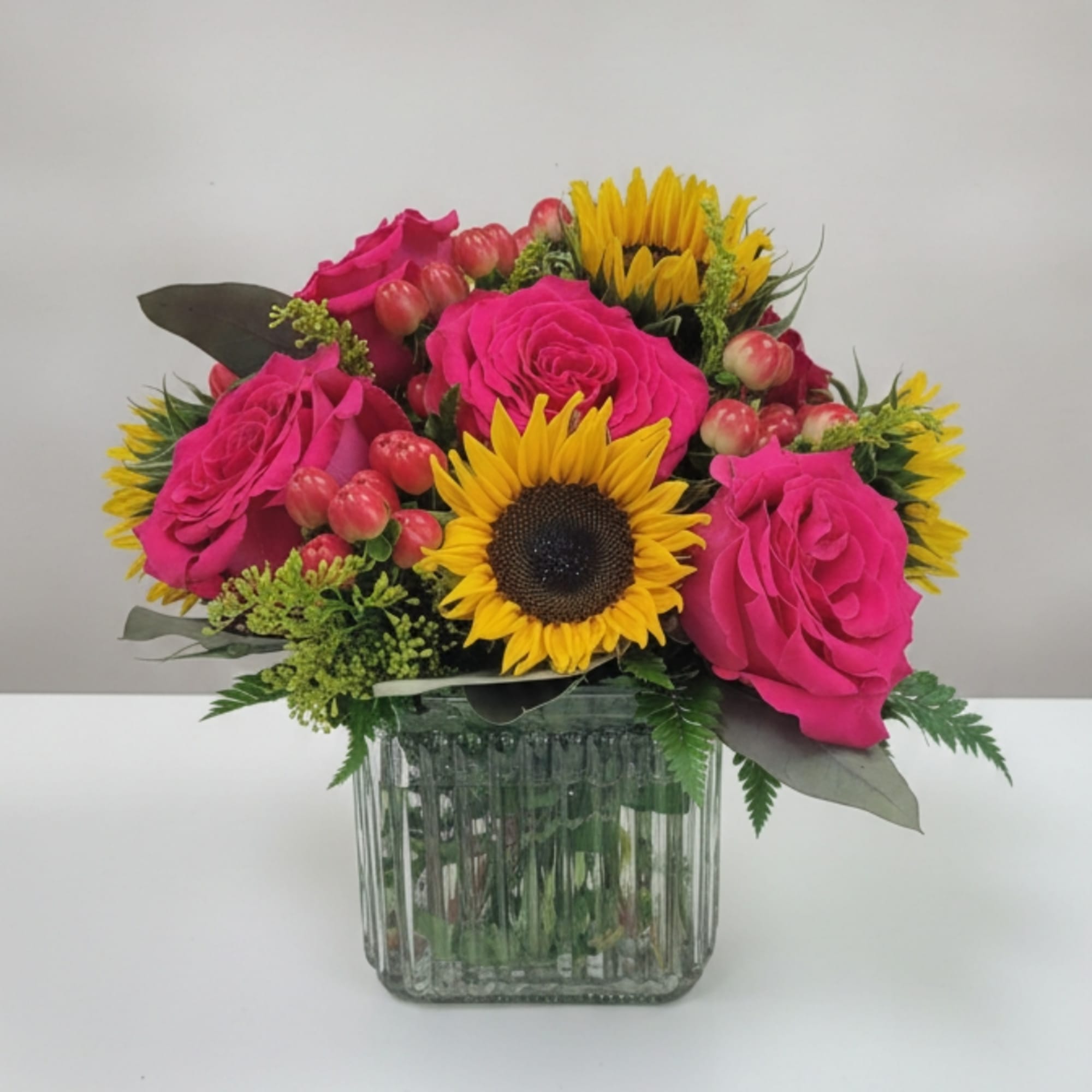 Pink roses and sunflowers arranged in a glass vase