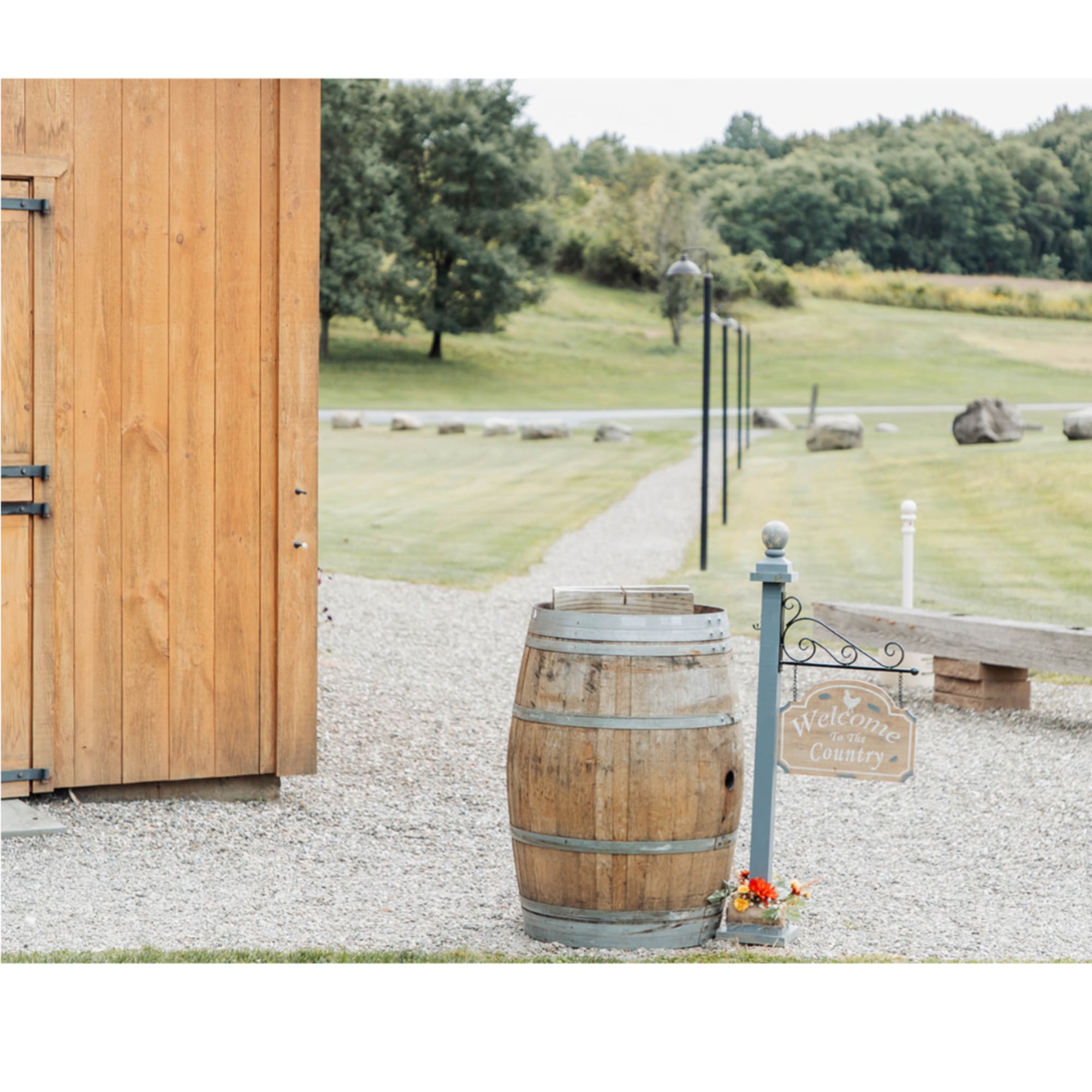 Rustic outdoor scene with a wooden barrel and a small flower arrangement by a welcome sign