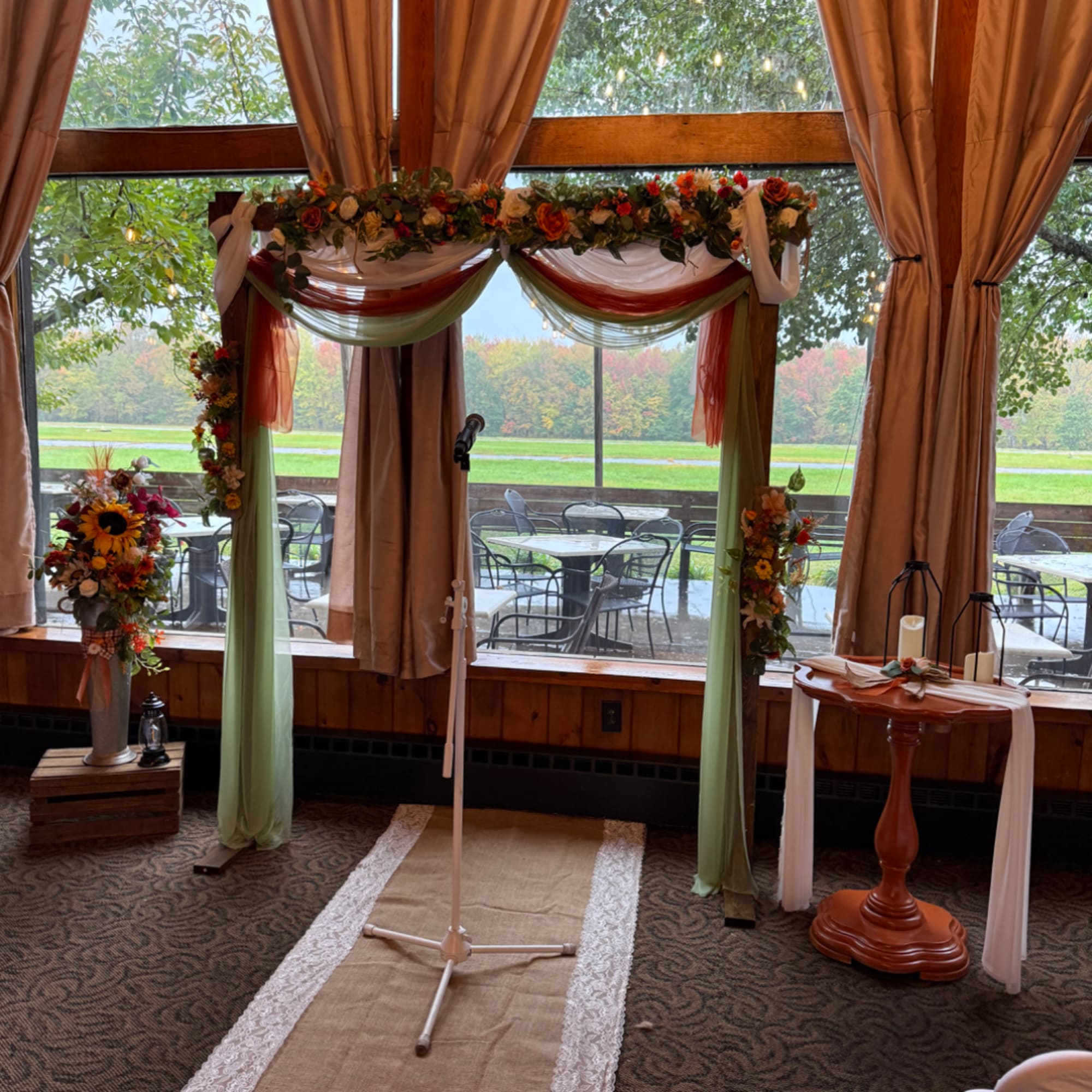 Wedding arch decorated with flowers and draped fabric in front of large windows