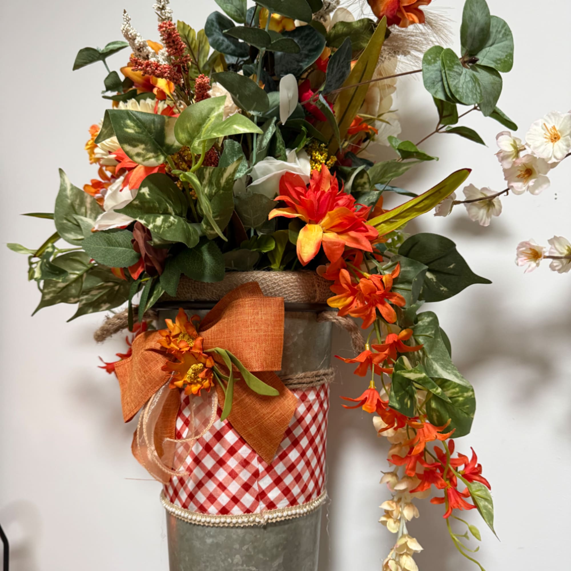 Orange floral arrangement in a metal container with a gingham wrap and bow