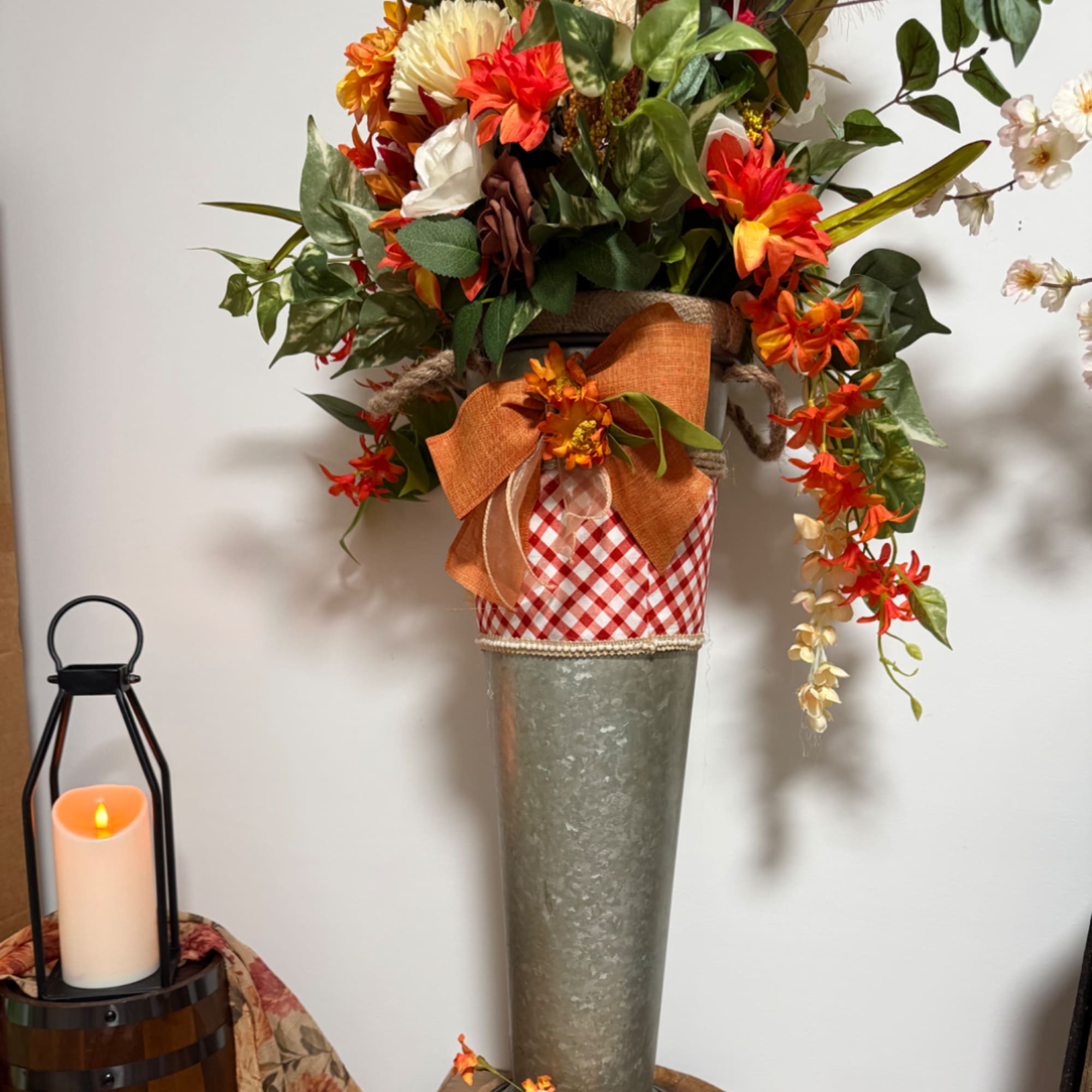 Tall autumn floral arrangement in a metal vase with orange ribbon and gingham wrap