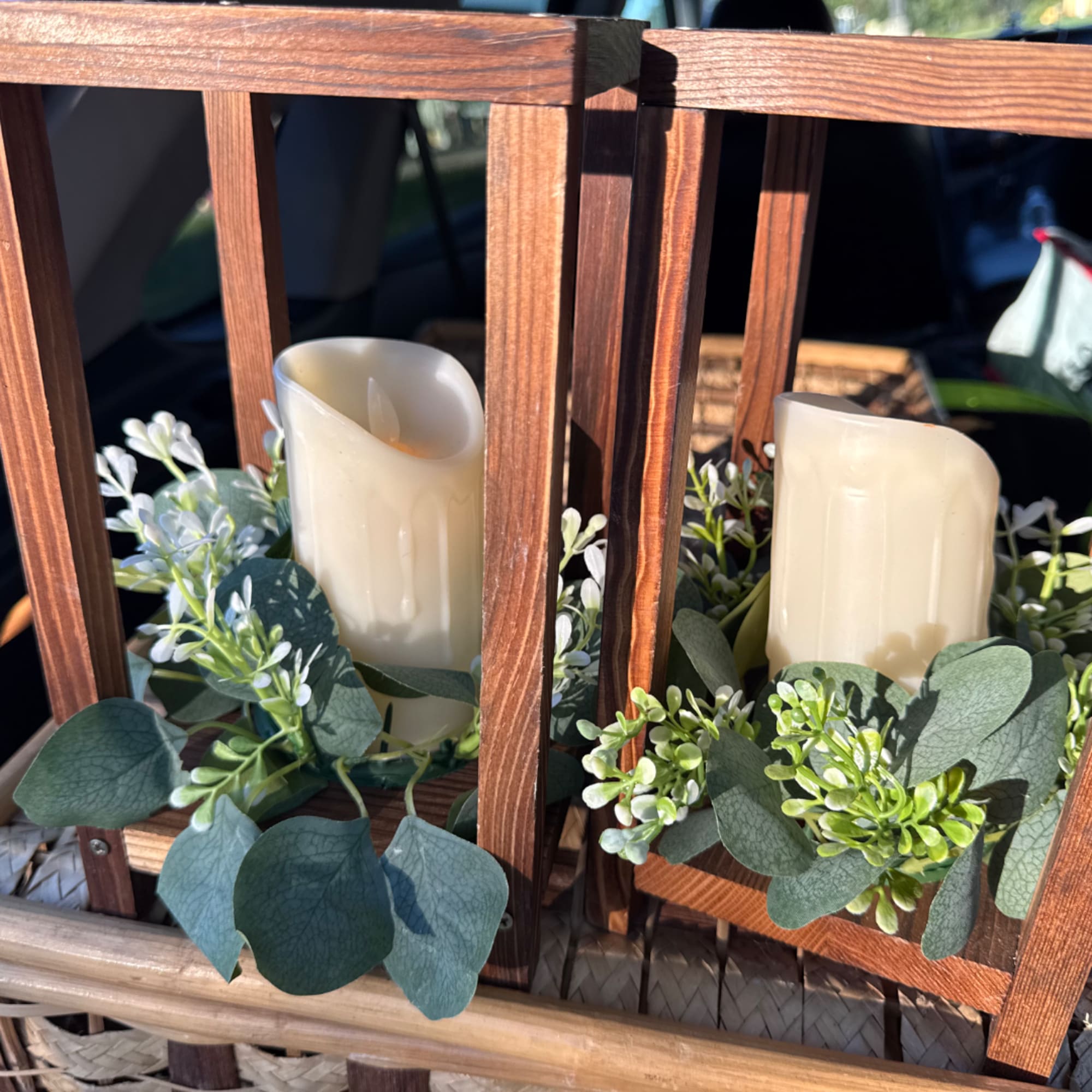 Two ivory candles in a wooden lantern with greenery accents