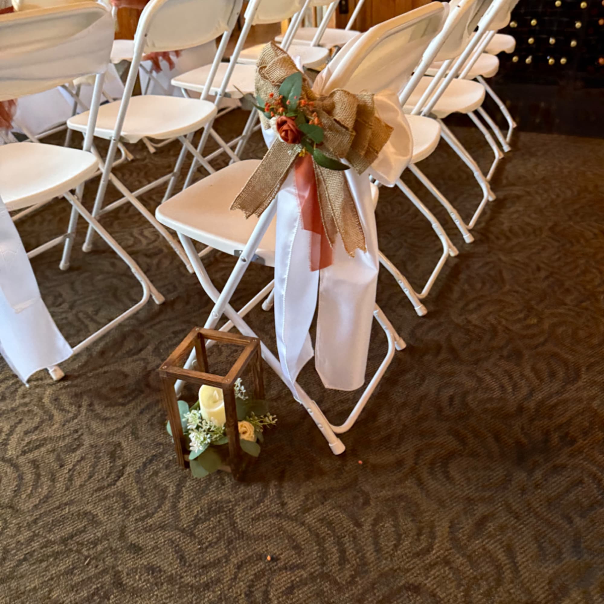 White folding chairs decorated with burlap bows and a lantern centerpiece