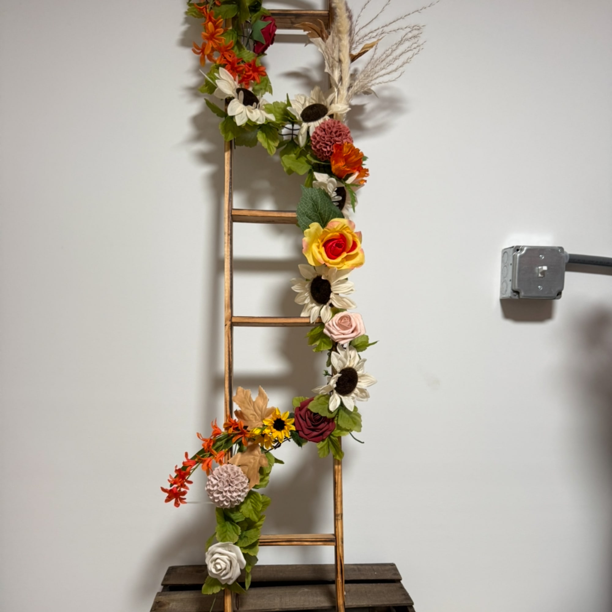 Floral garland wrapped around a wooden ladder with mixed blooms