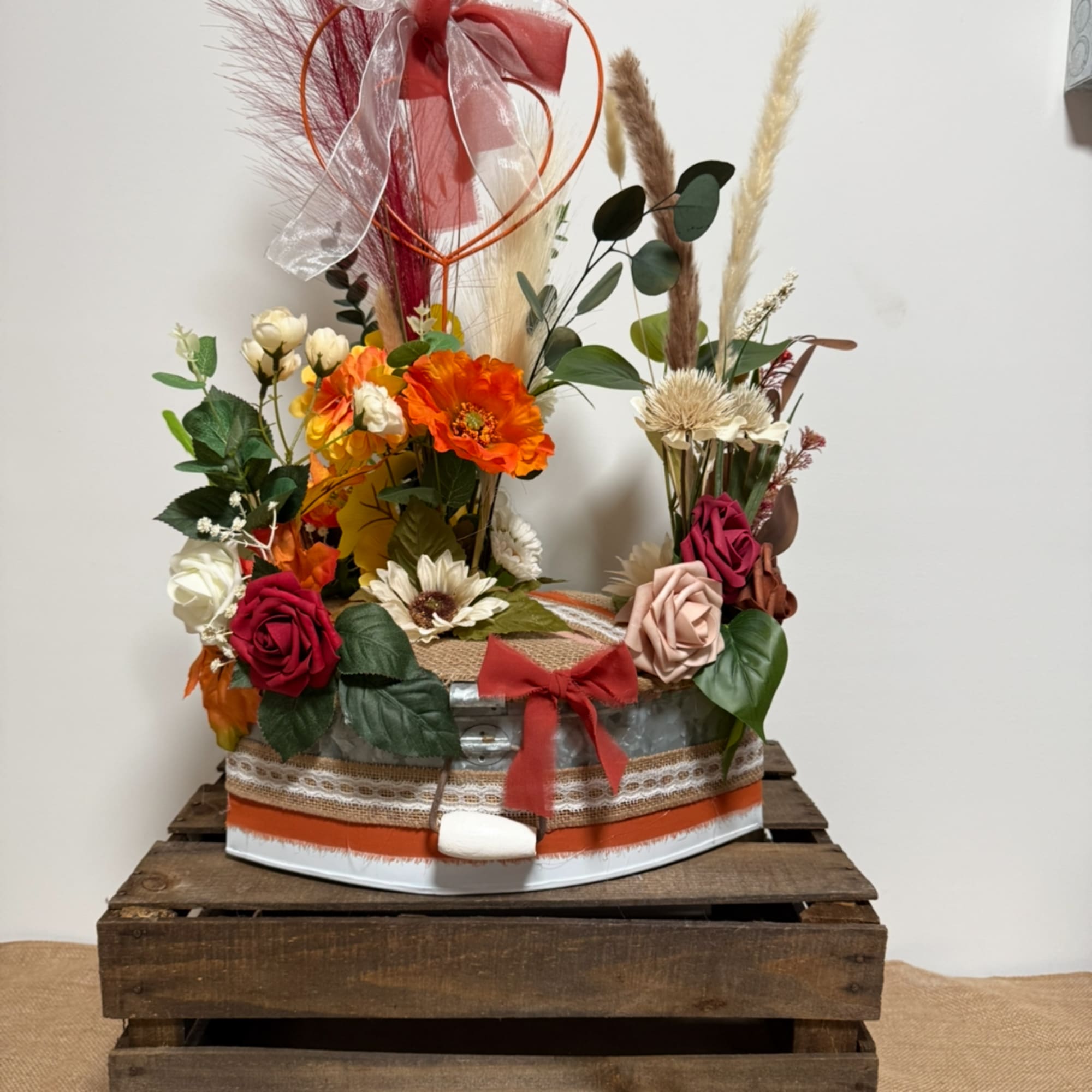 Mixed floral arrangement in a decorated metal container with ribbon and dried grasses