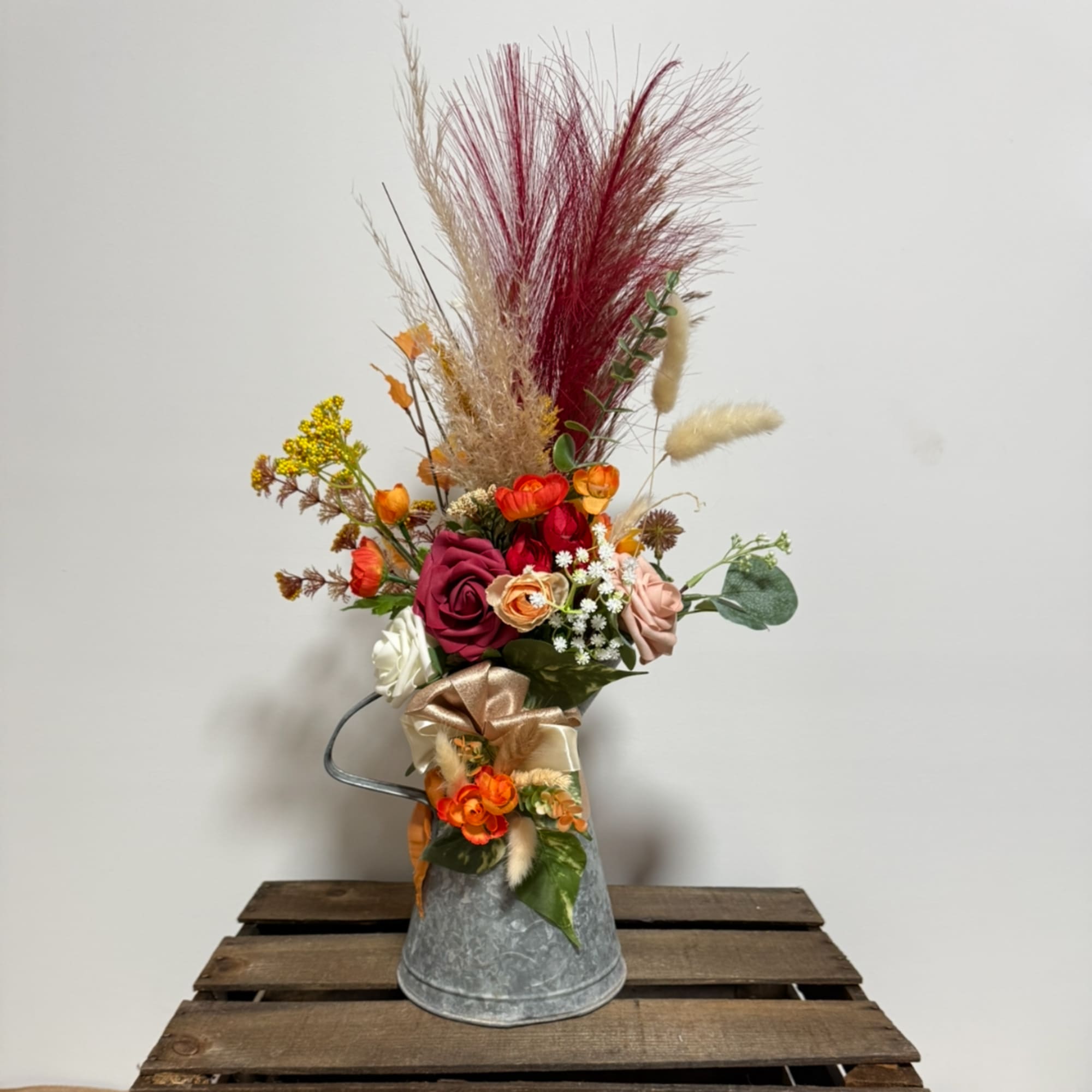 Tall floral arrangement in a metal bucket with roses and dried grasses