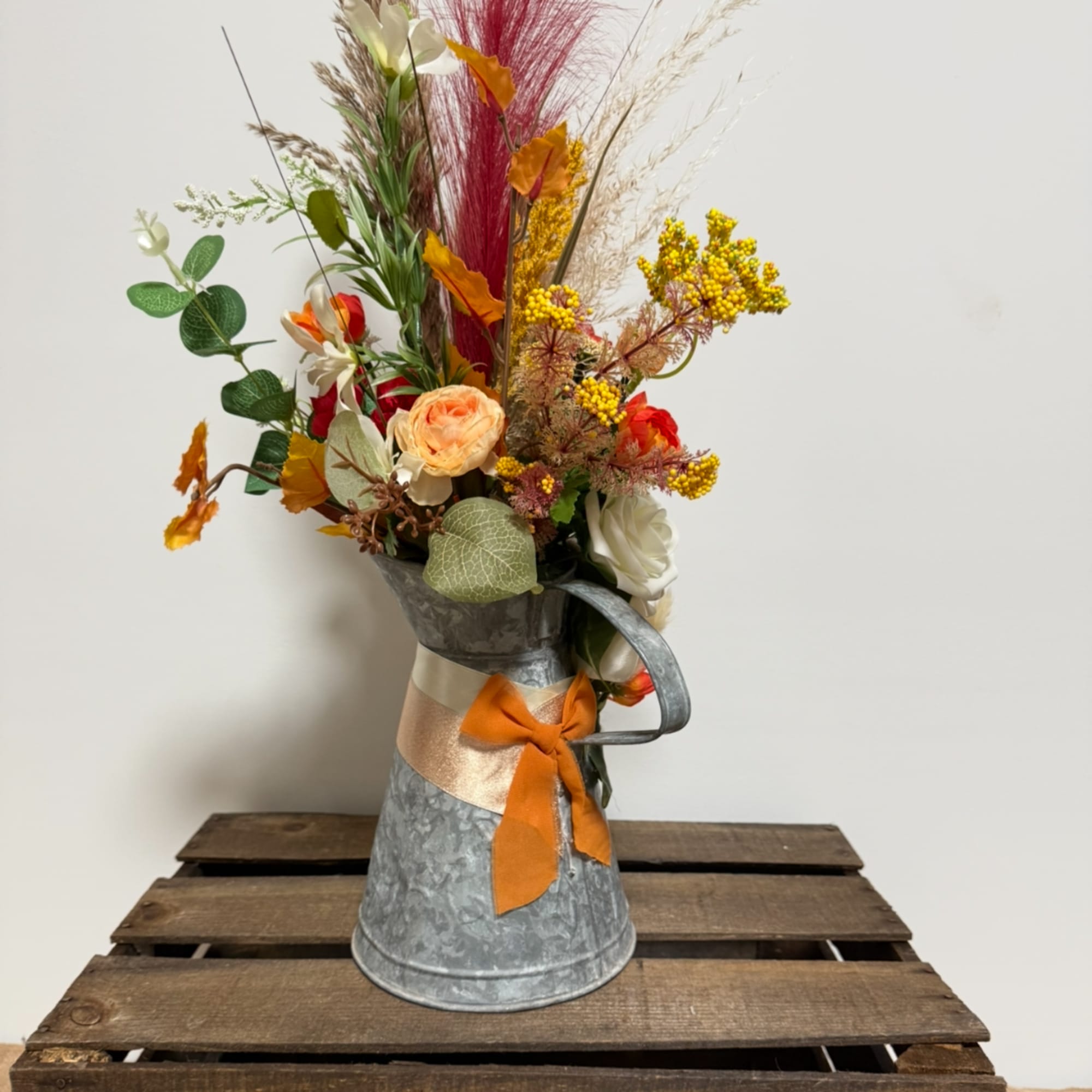 Tall floral arrangement in a metal pitcher with orange ribbon