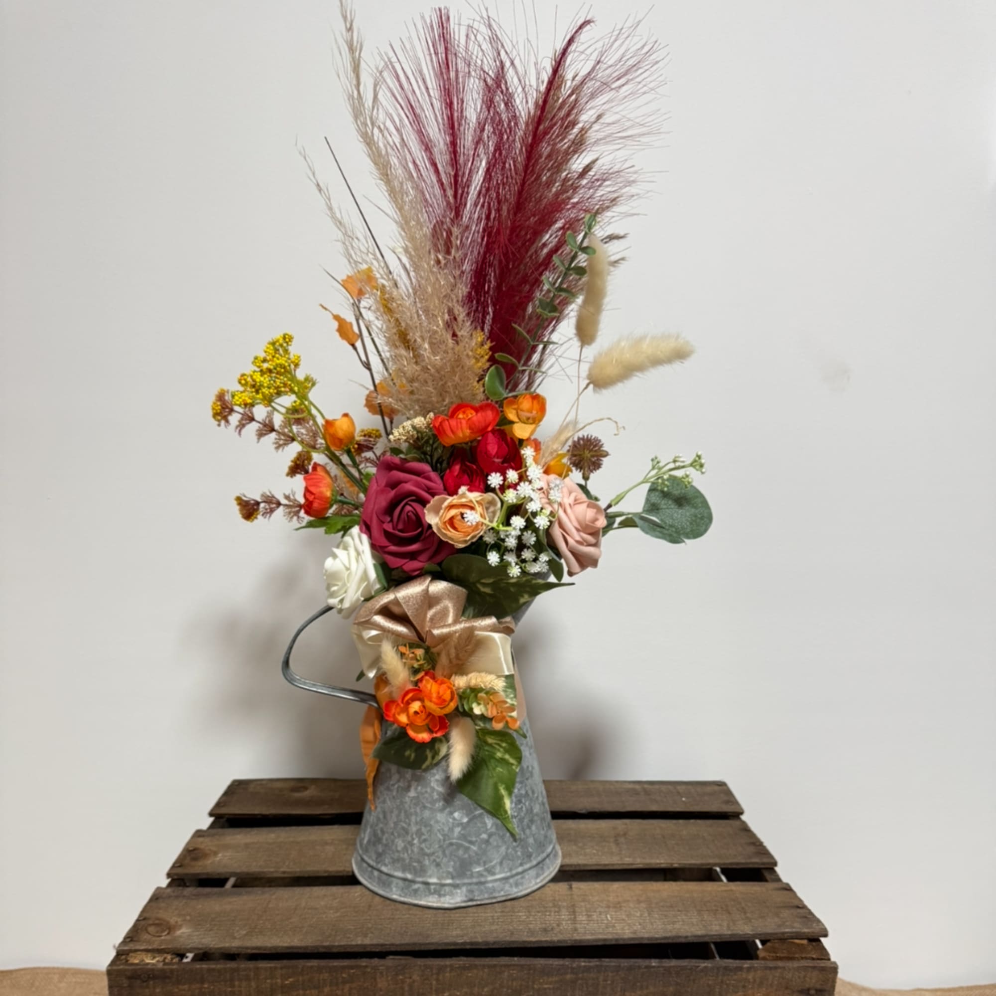 Tall floral arrangement in a metal pitcher with roses and dried grasses