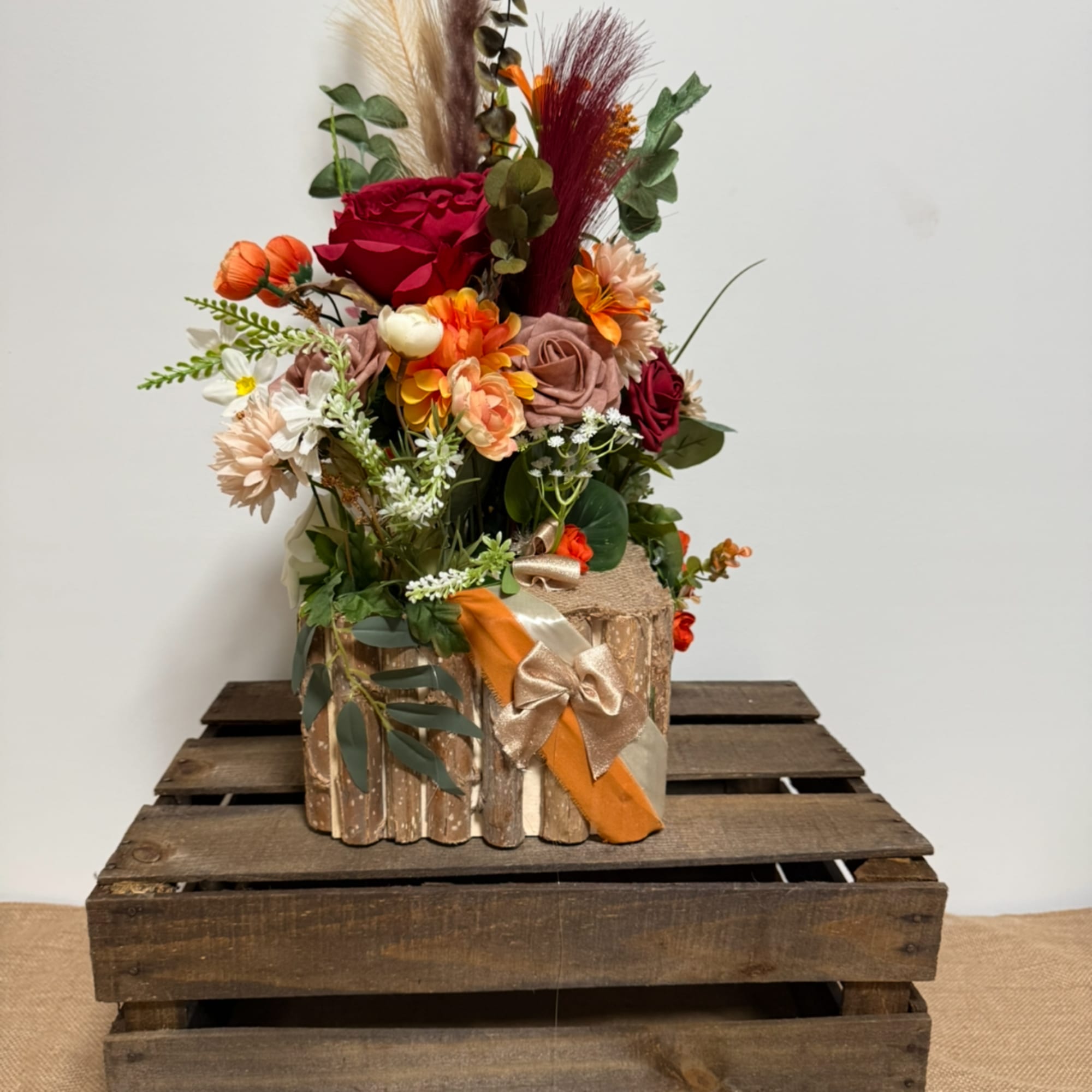 Mixed floral arrangement in a rustic wooden container with a ribbon bow