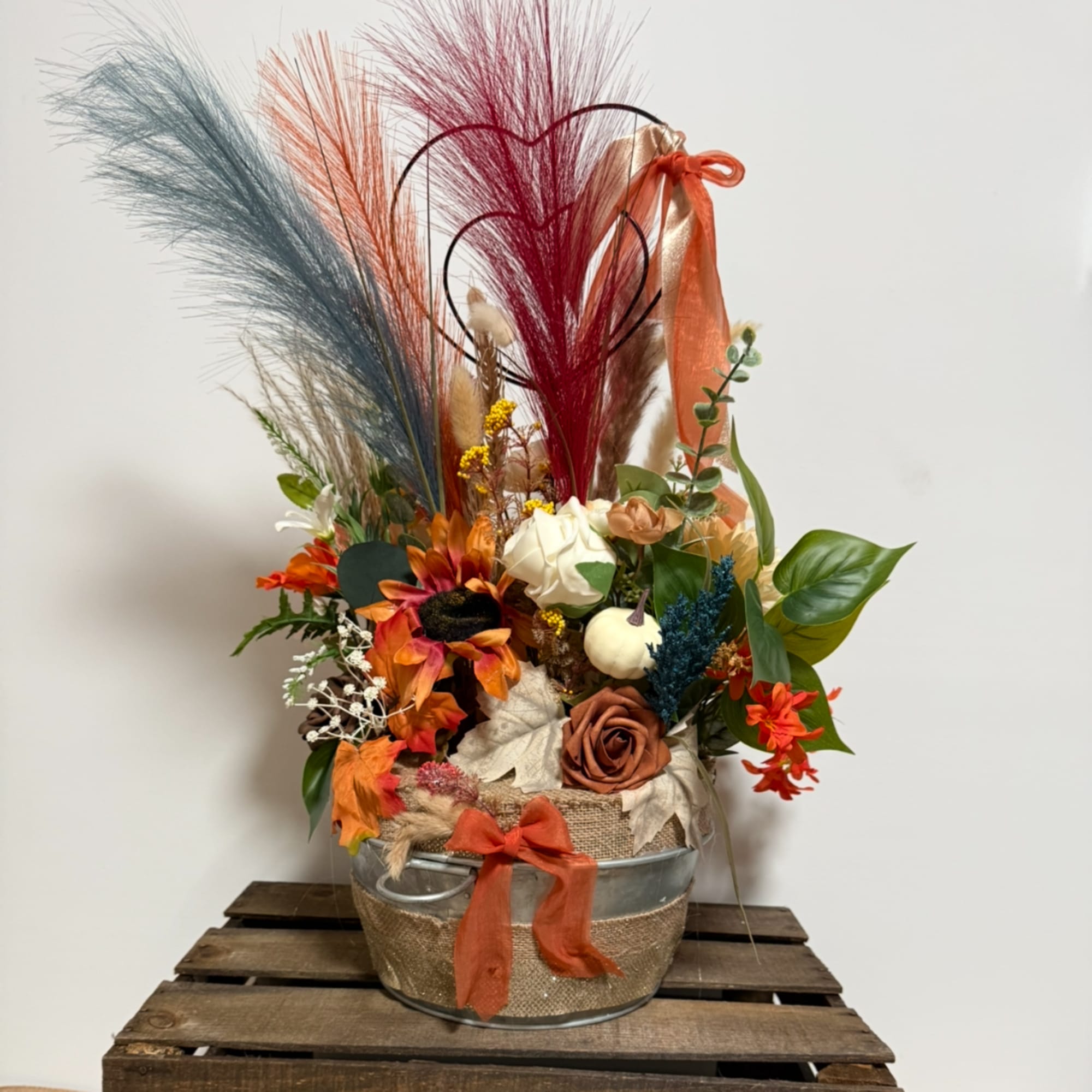 Autumn floral arrangement in a metal bucket with tall dried grasses and orange accents