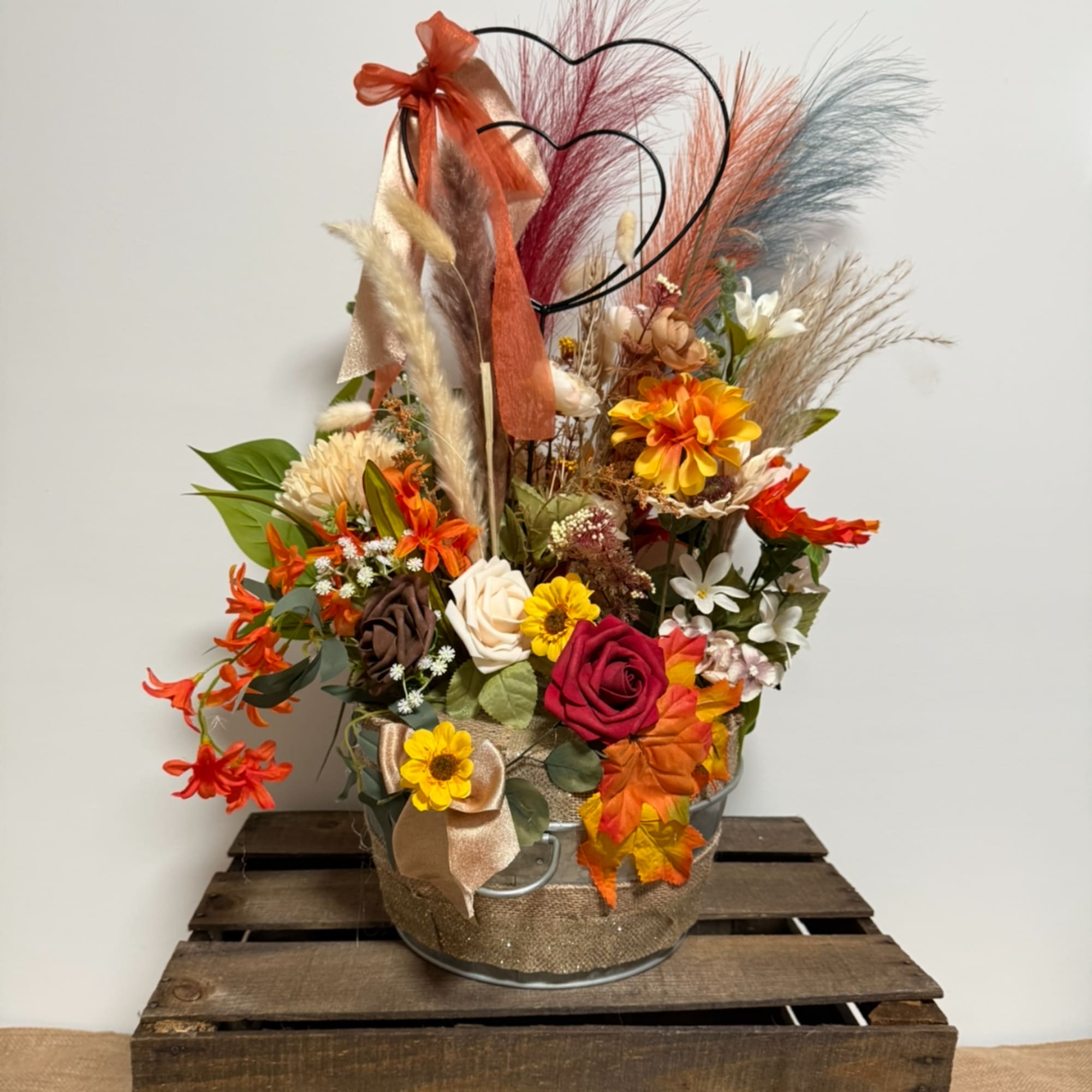 Autumn floral arrangement in a metal bucket with heart picks and ribbon