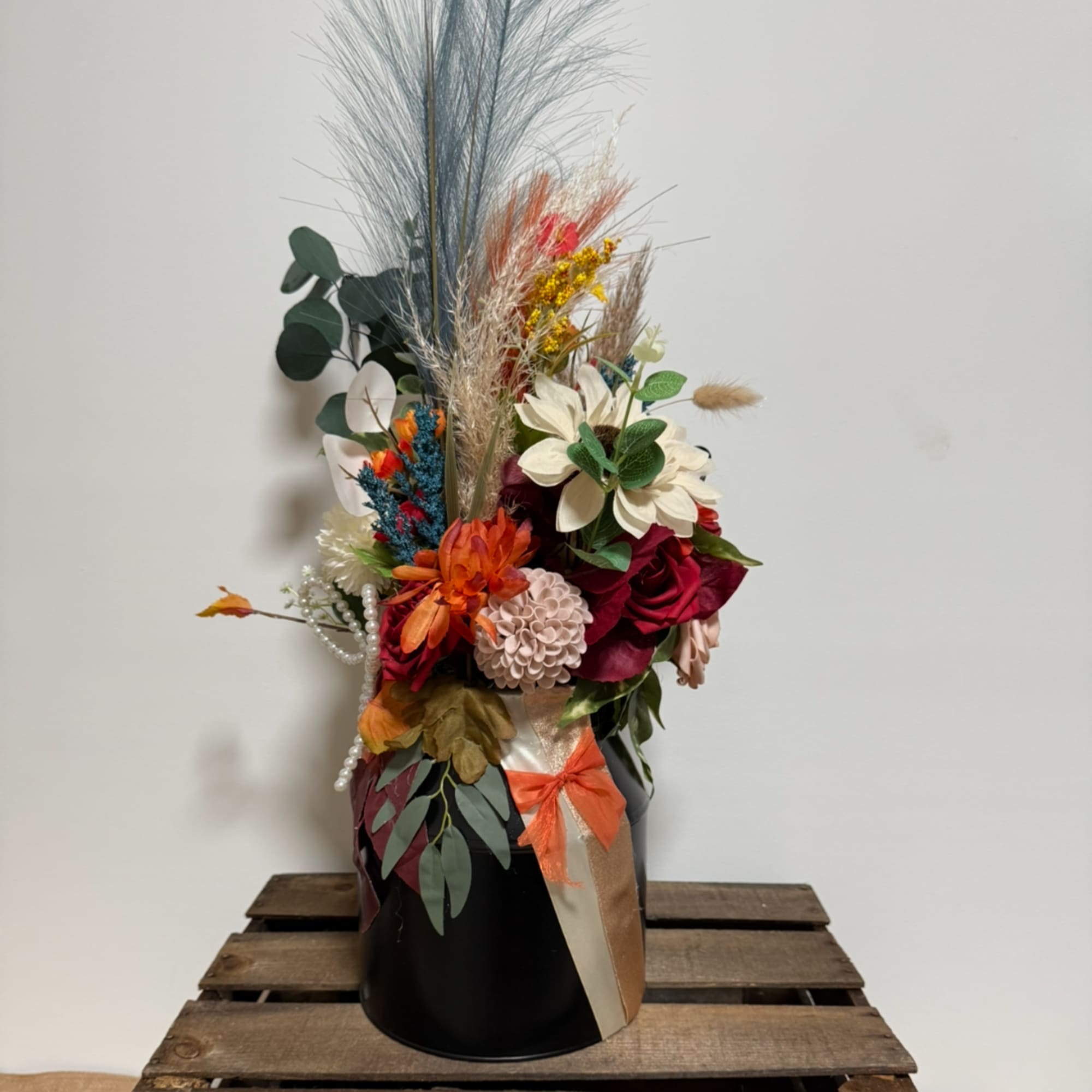 Tall mixed floral arrangement in a black vase with dried grasses and ribbon