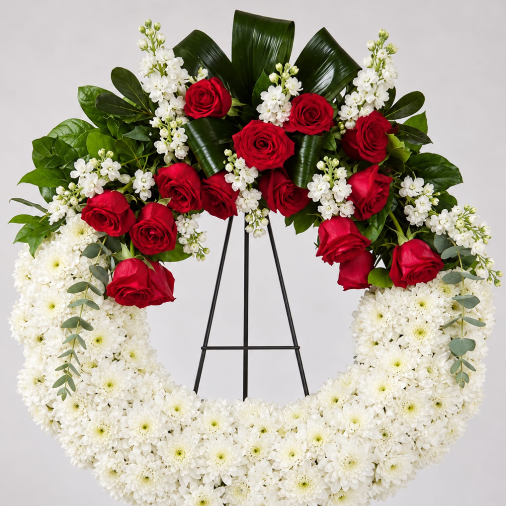 Red roses and white flowers arranged in a circular wreath on a stand