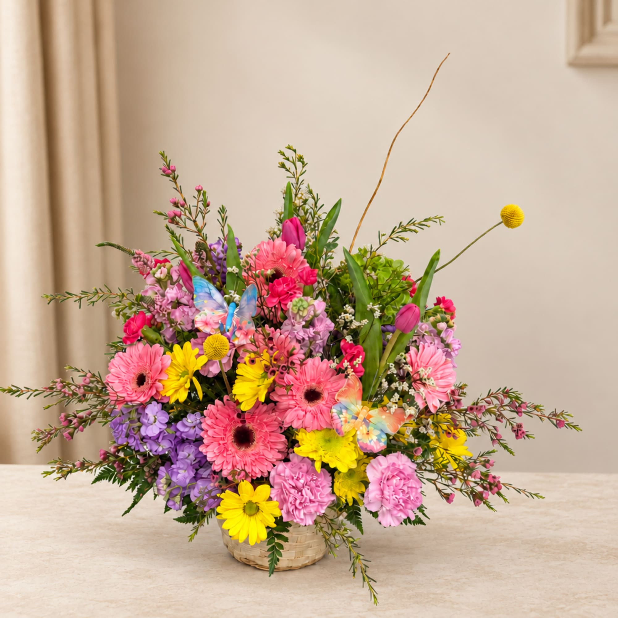 Colorful mixed flower arrangement in a wicker basket with butterfly picks