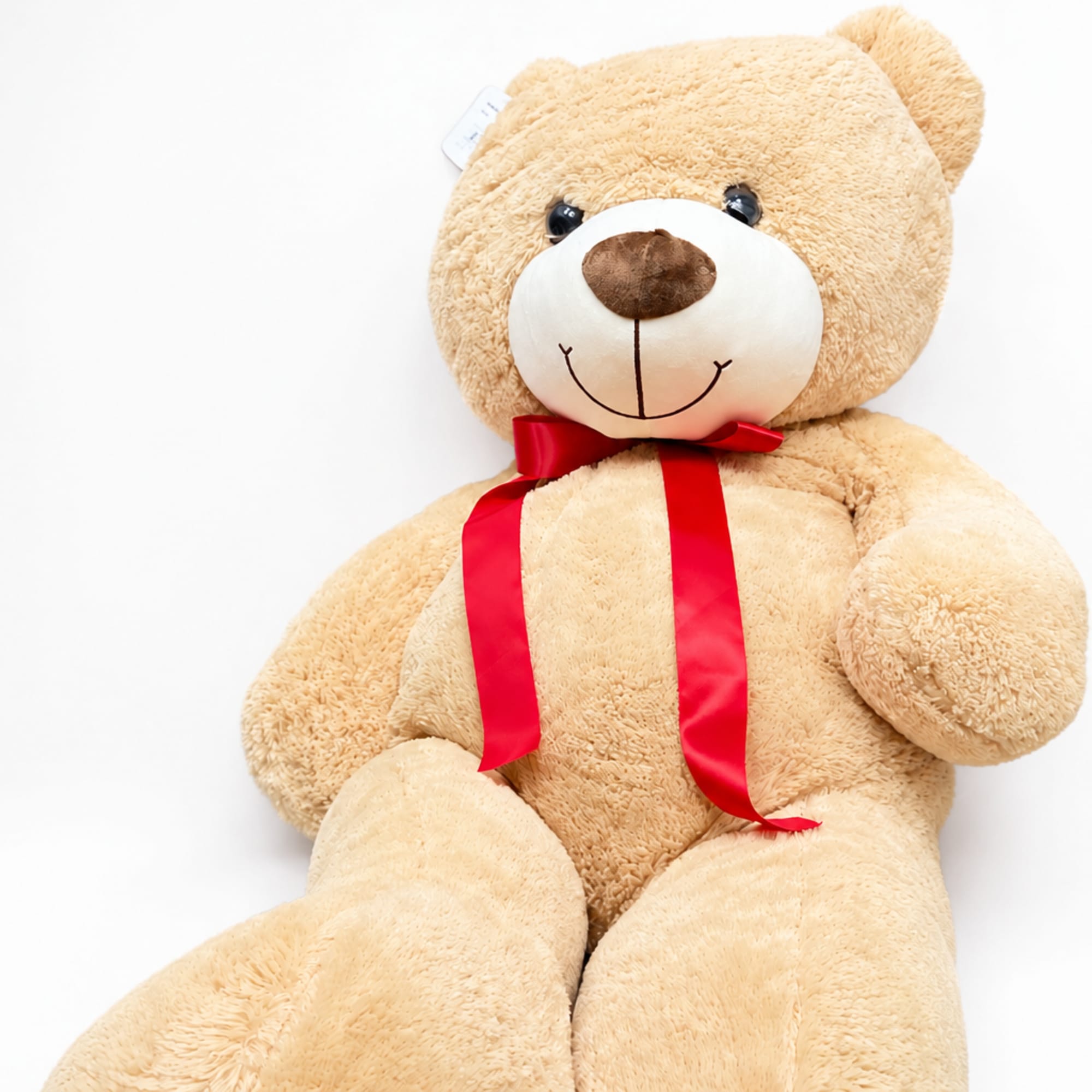 Large beige teddy bear with a red ribbon bow on a white background