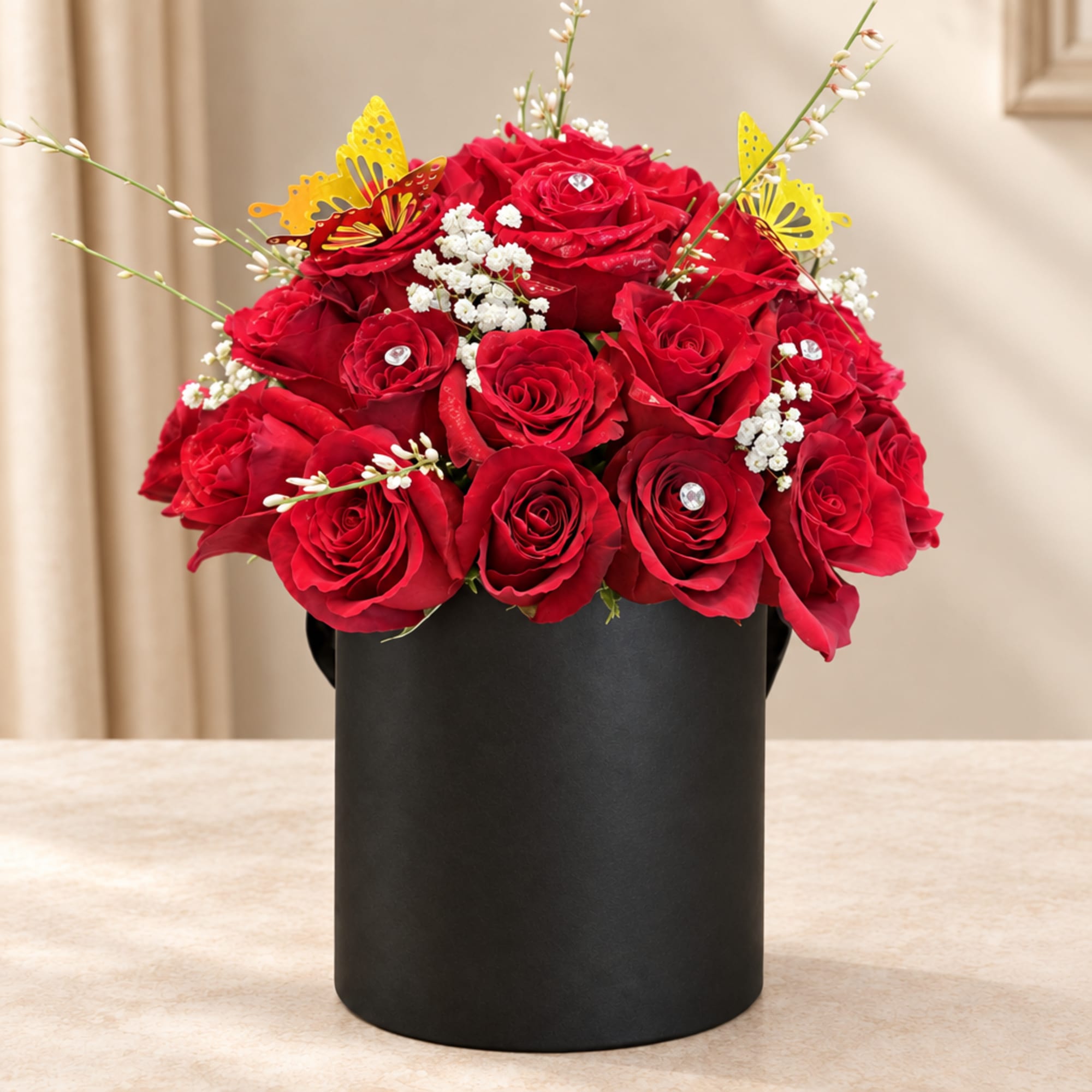 Red rose arrangement in a black cylindrical box with butterfly picks
