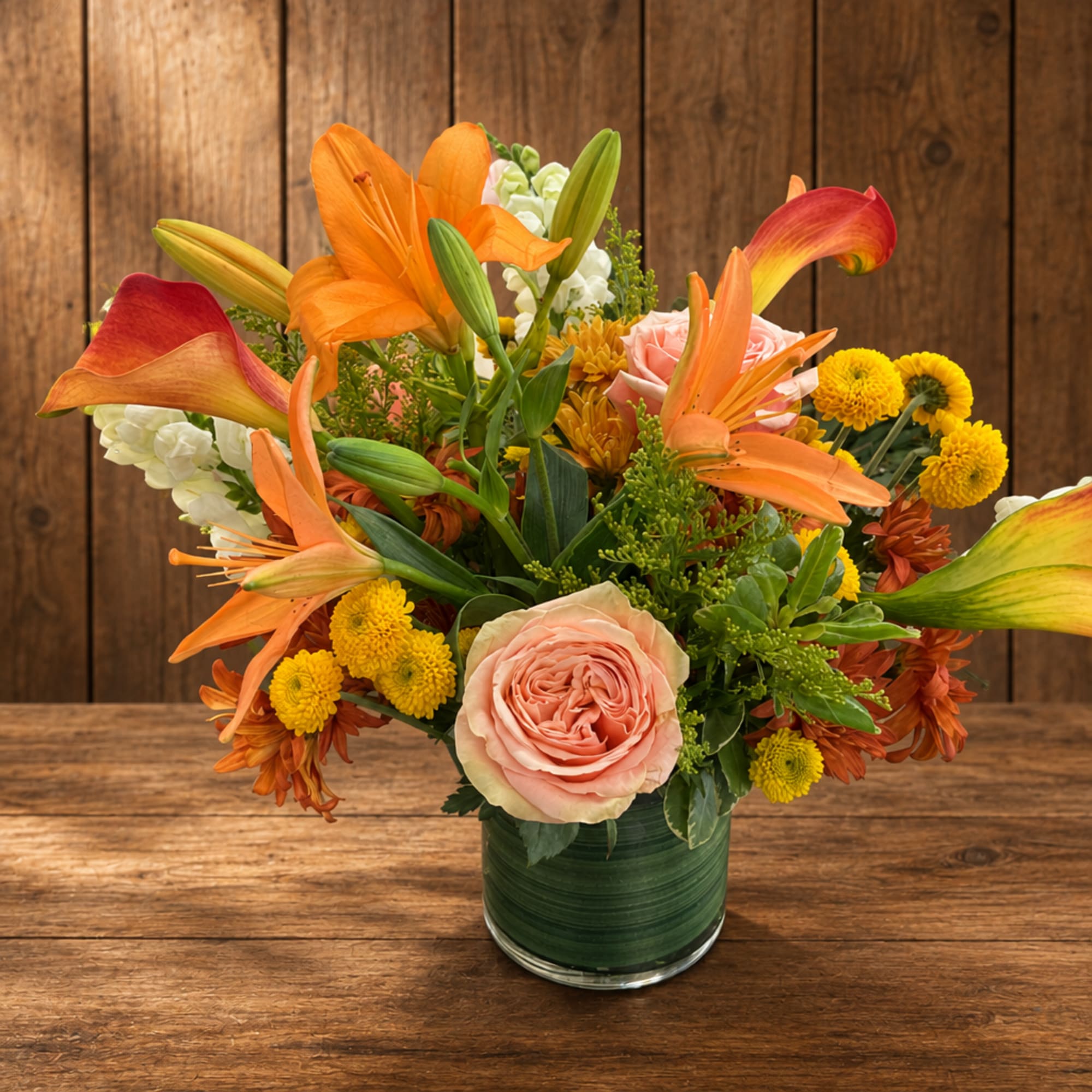 Mixed bouquet with orange lilies, pink roses, and yellow mums in a green glass vase