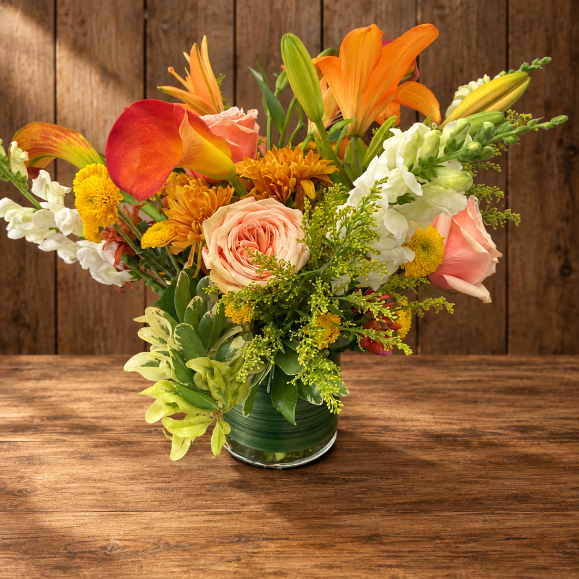 Mixed bouquet of orange lilies, pink roses, and yellow mums in a glass vase