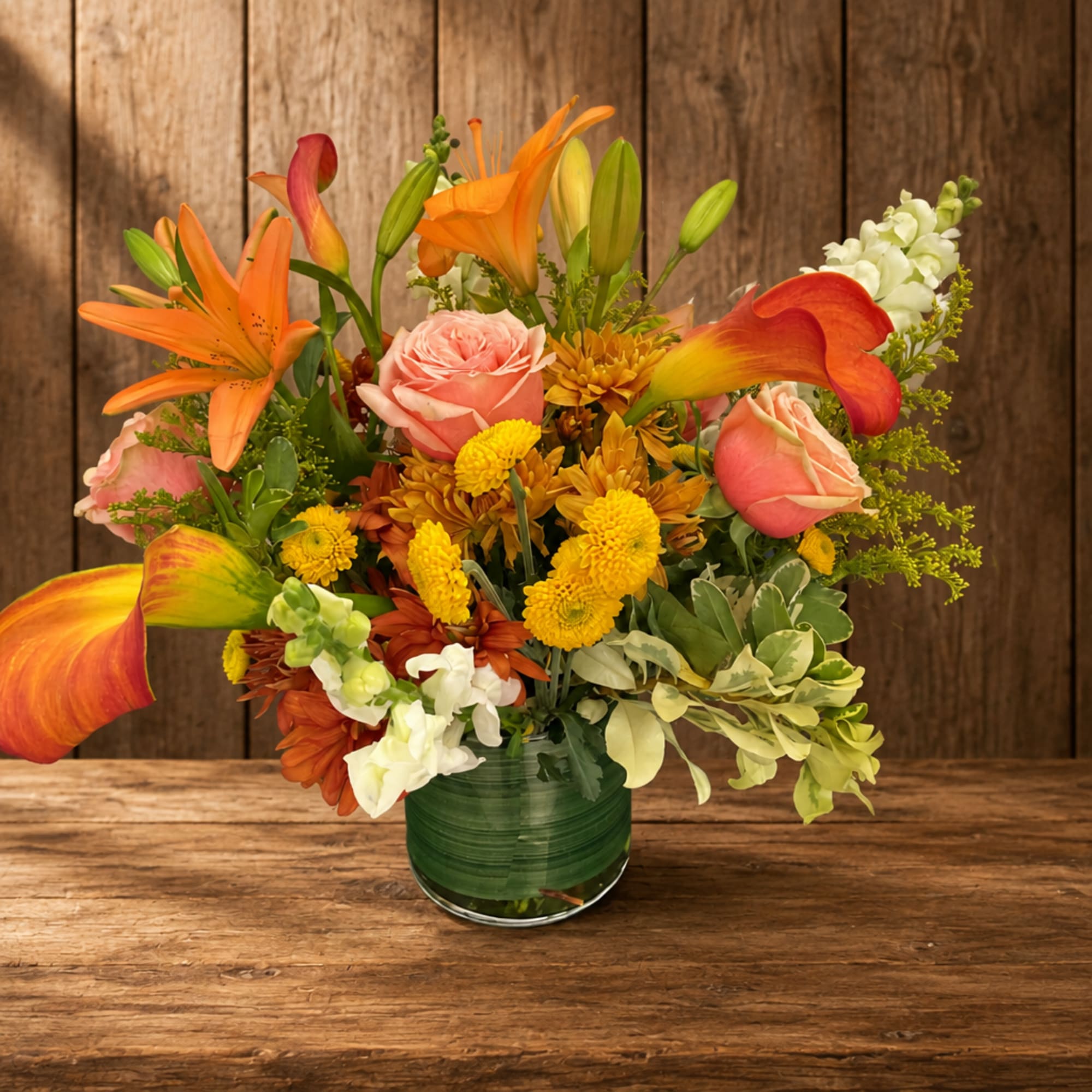Orange lilies, pink roses, and yellow mums in a green glass vase