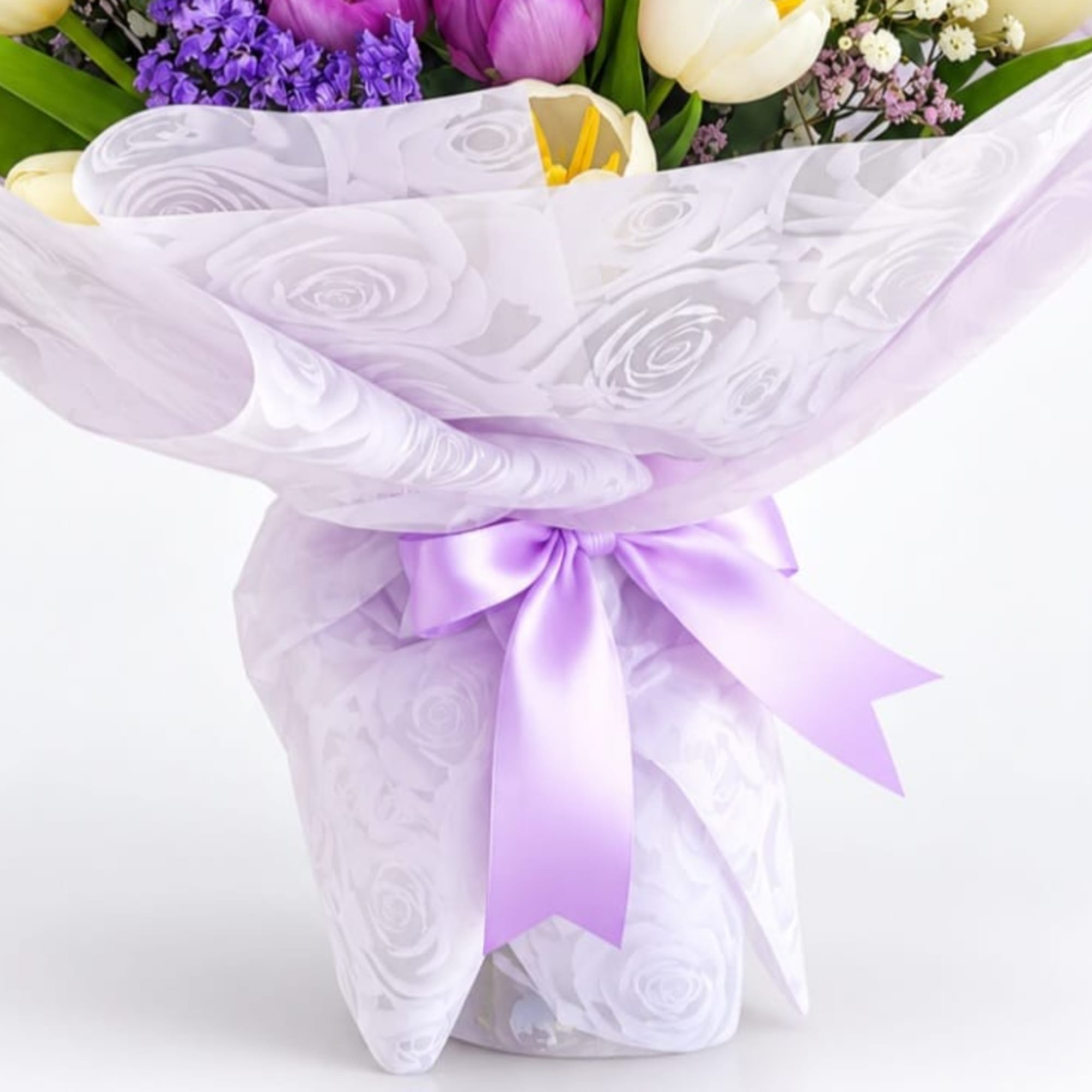 Bouquet of mixed flowers wrapped in white paper with a lavender ribbon