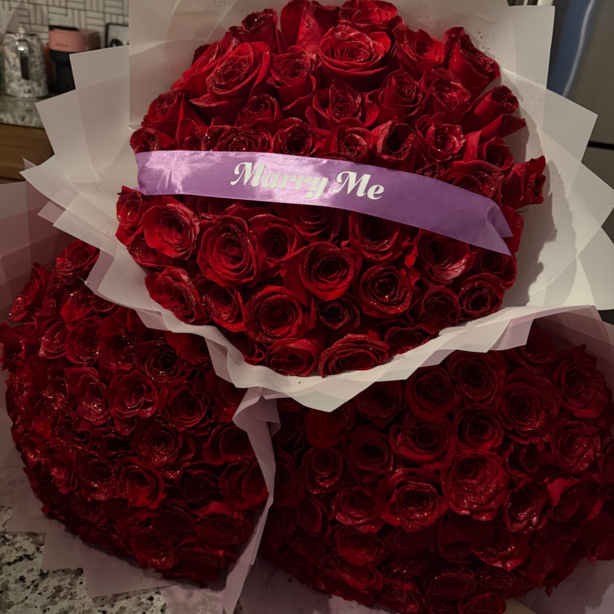 Large bouquet of red roses wrapped in white paper with a purple ribbon