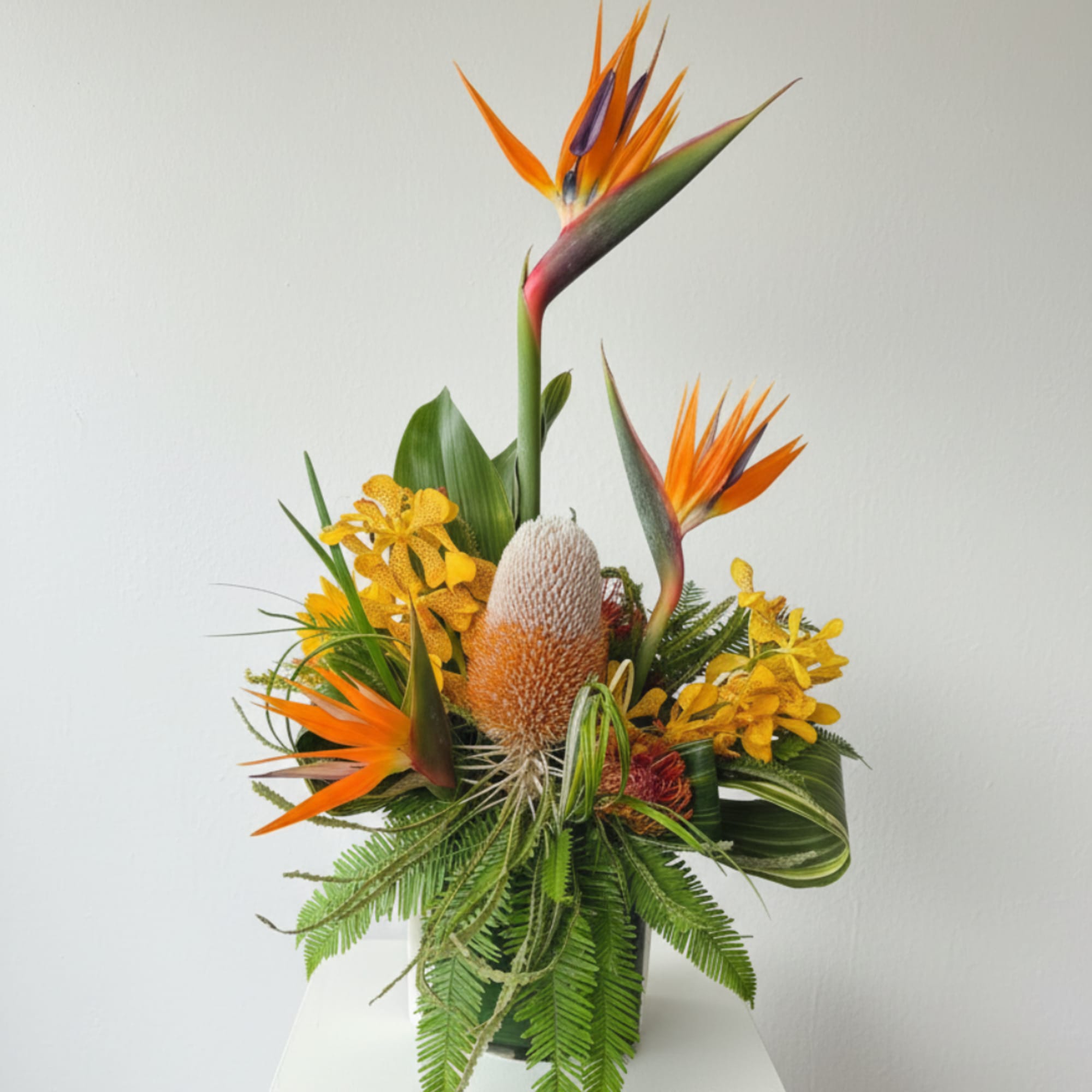 Tropical arrangement with orange bird-of-paradise and yellow orchids in a vase