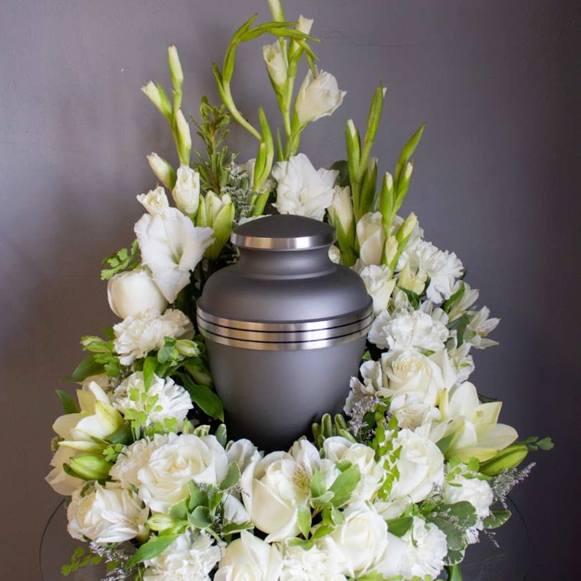 Cremation urn encircled by white roses, lilies, and carnations in a wreath-style arrangement