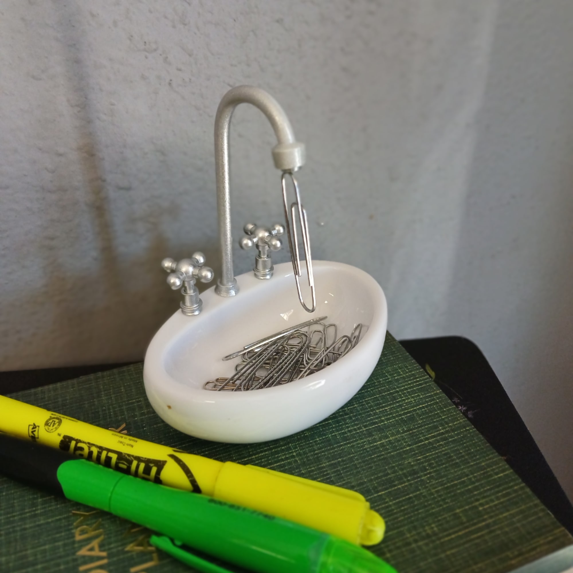 Miniature sink-shaped paperclip holder with paperclips and pens nearby