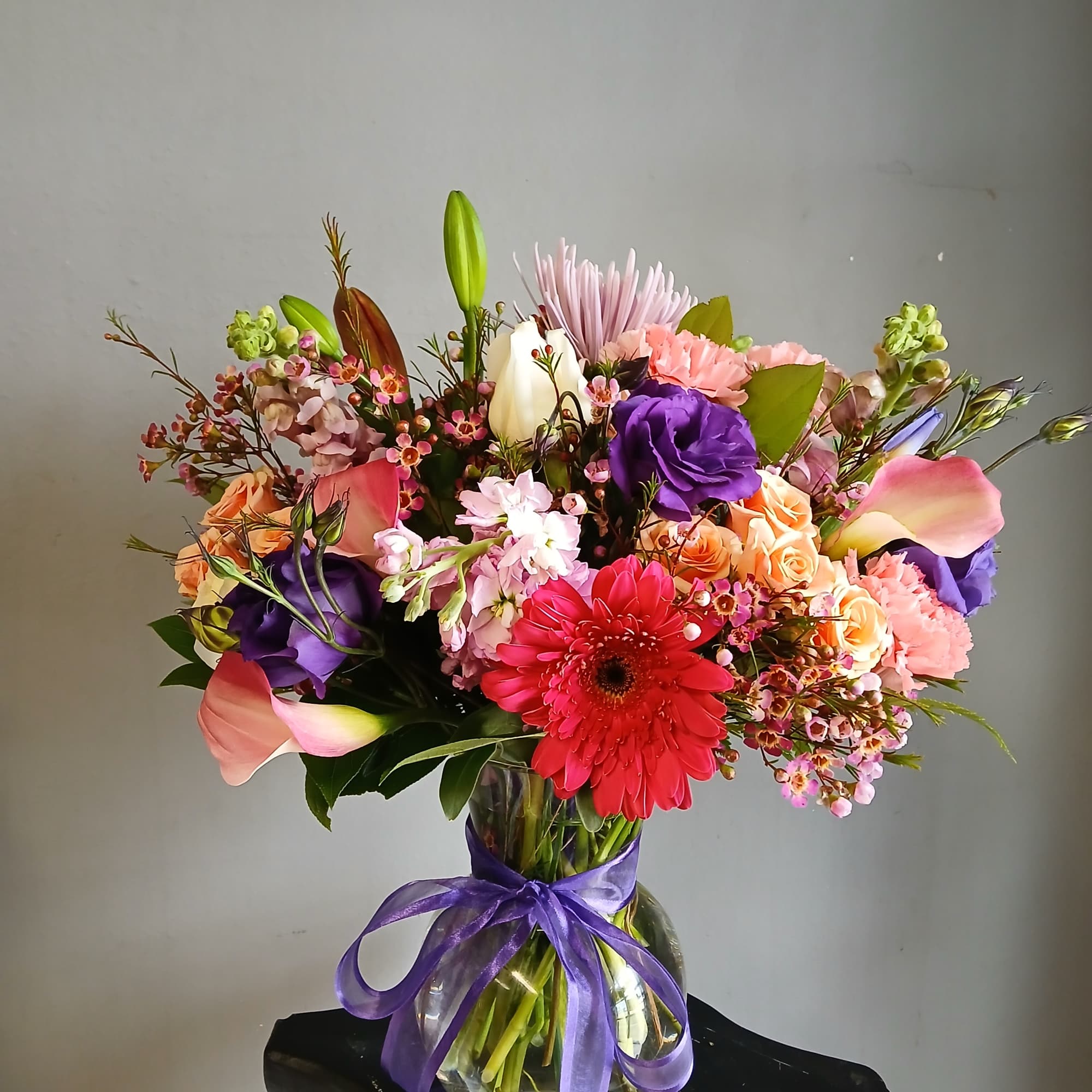 Colorful mixed bouquet in a glass vase tied with a purple ribbon
