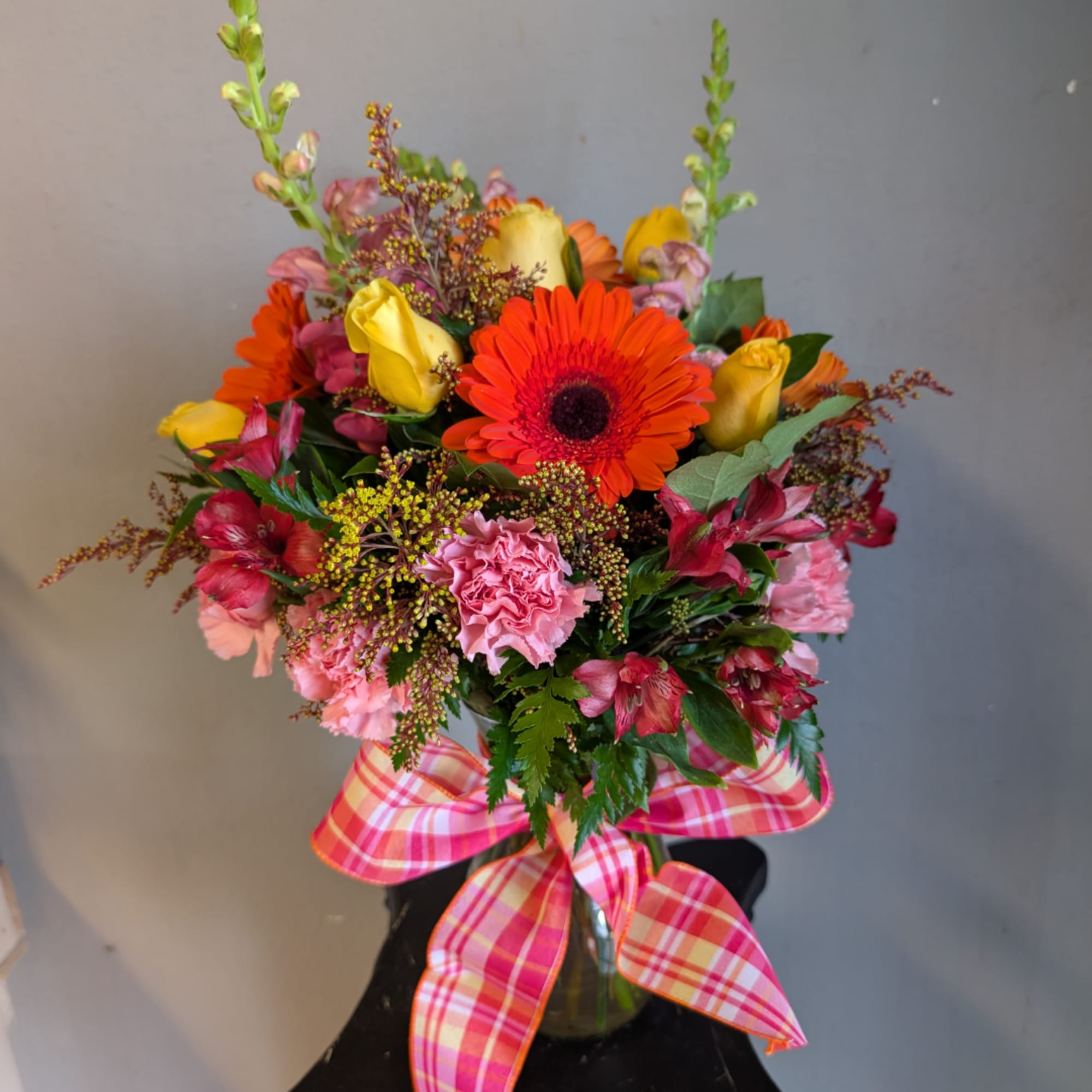 Bright mixed bouquet in a glass vase with a plaid ribbon bow