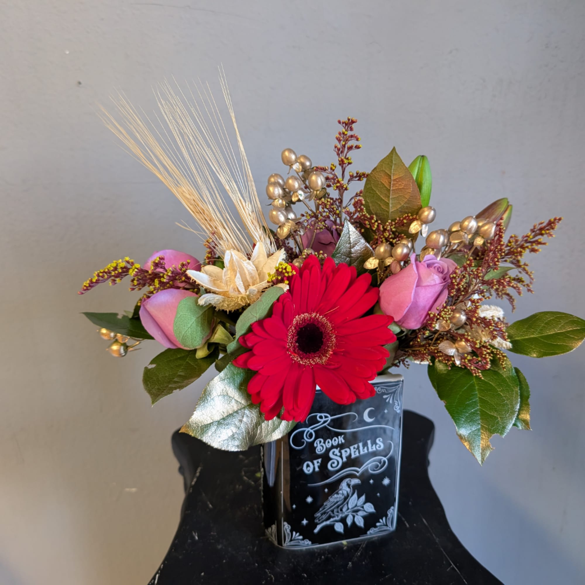 Mixed floral arrangement in a black book-shaped vase with a red gerbera daisy and pink roses.