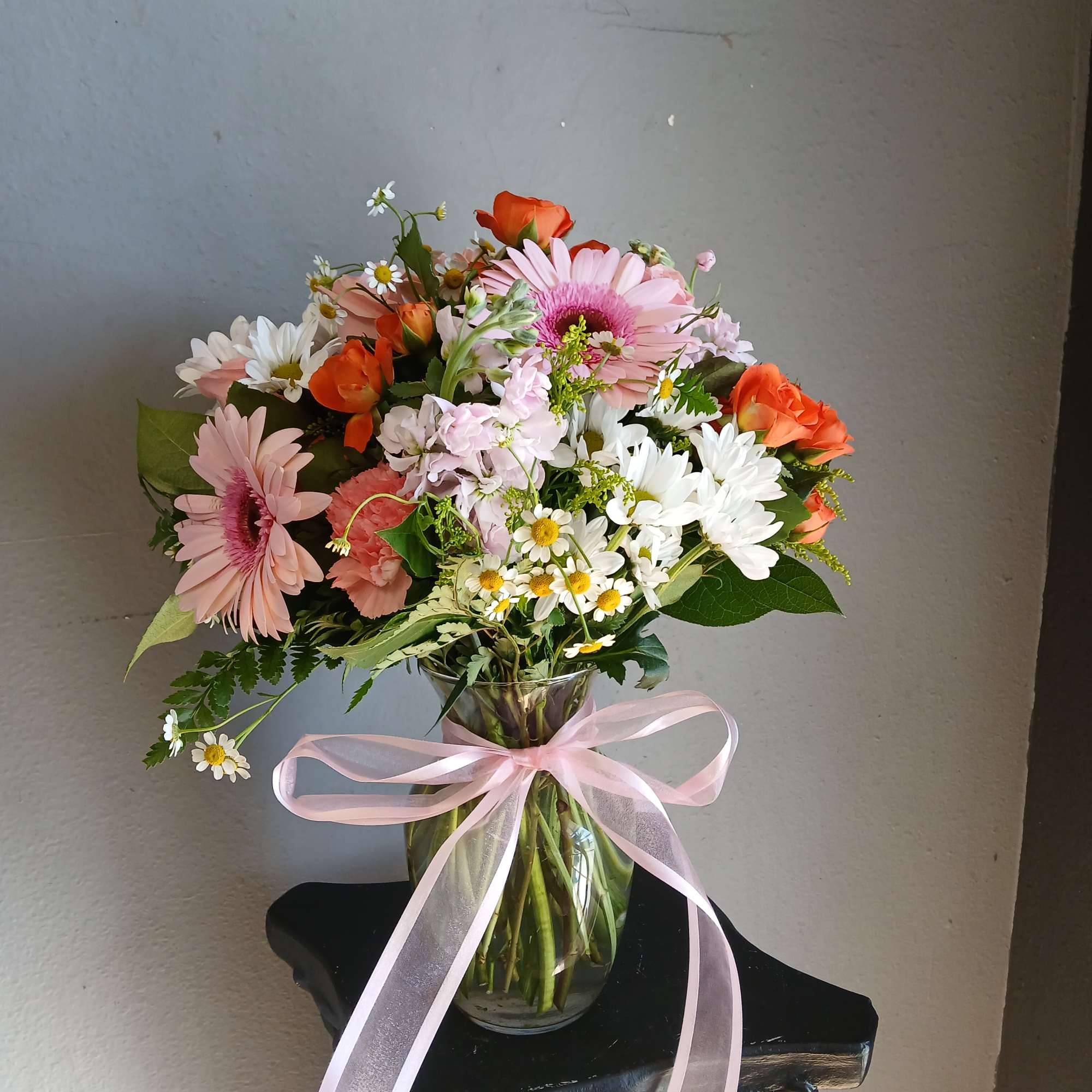 Mixed pink, white, and orange flowers in a glass vase with a pink ribbon