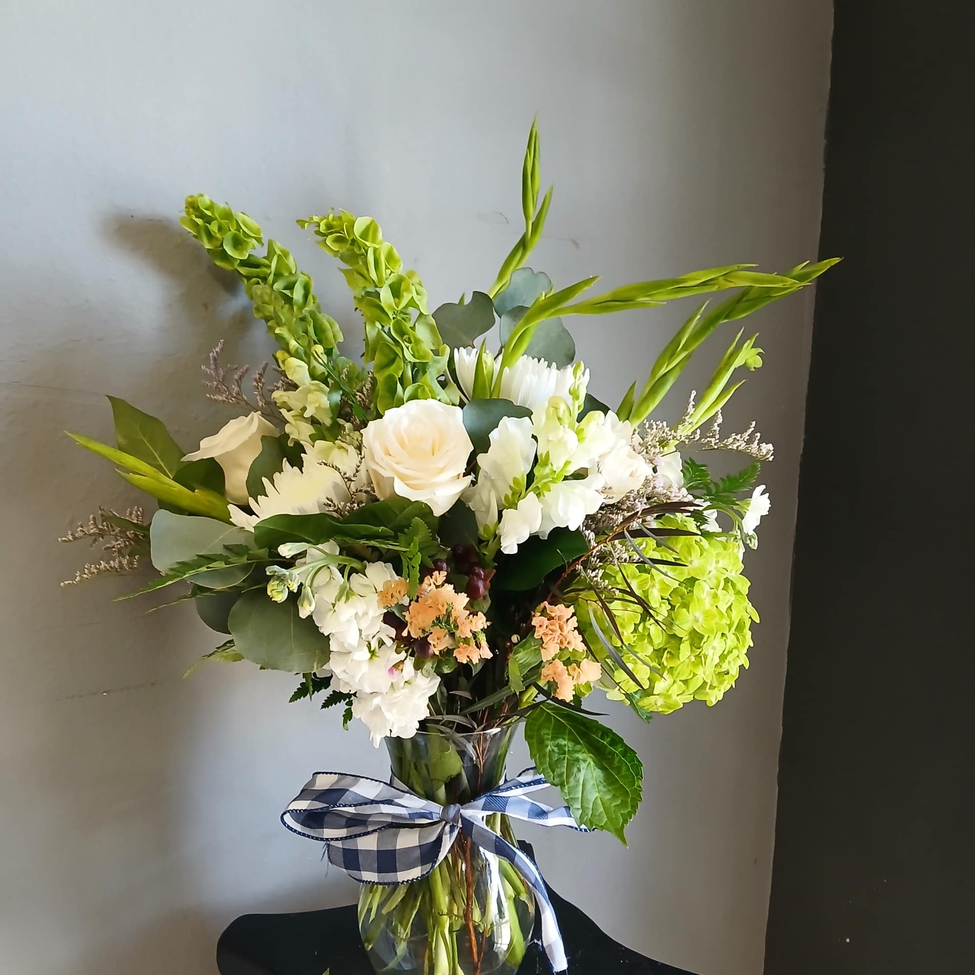 White and green floral arrangement in a glass vase with a plaid ribbon