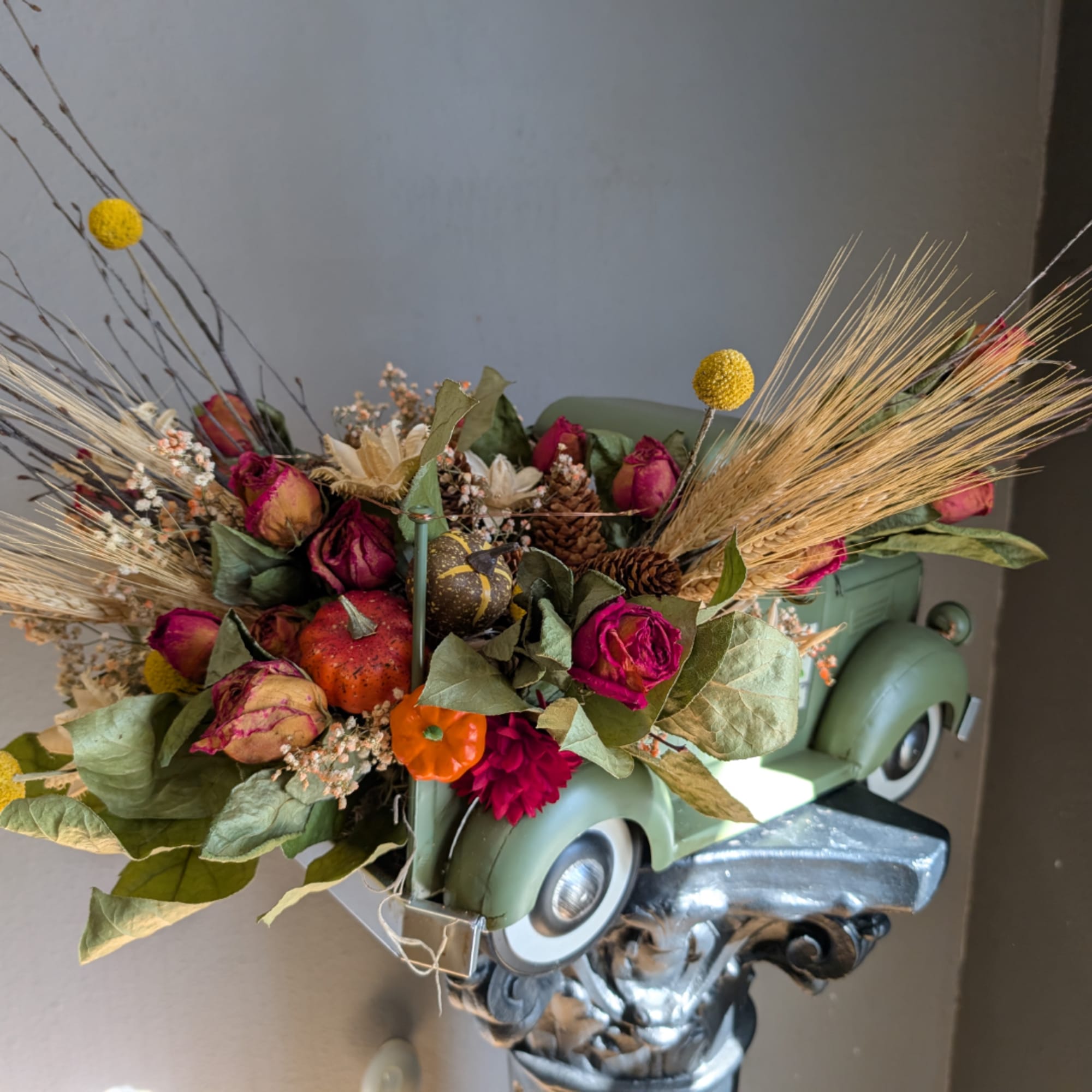 Floral arrangement in a vintage green truck container with dried flowers and wheat