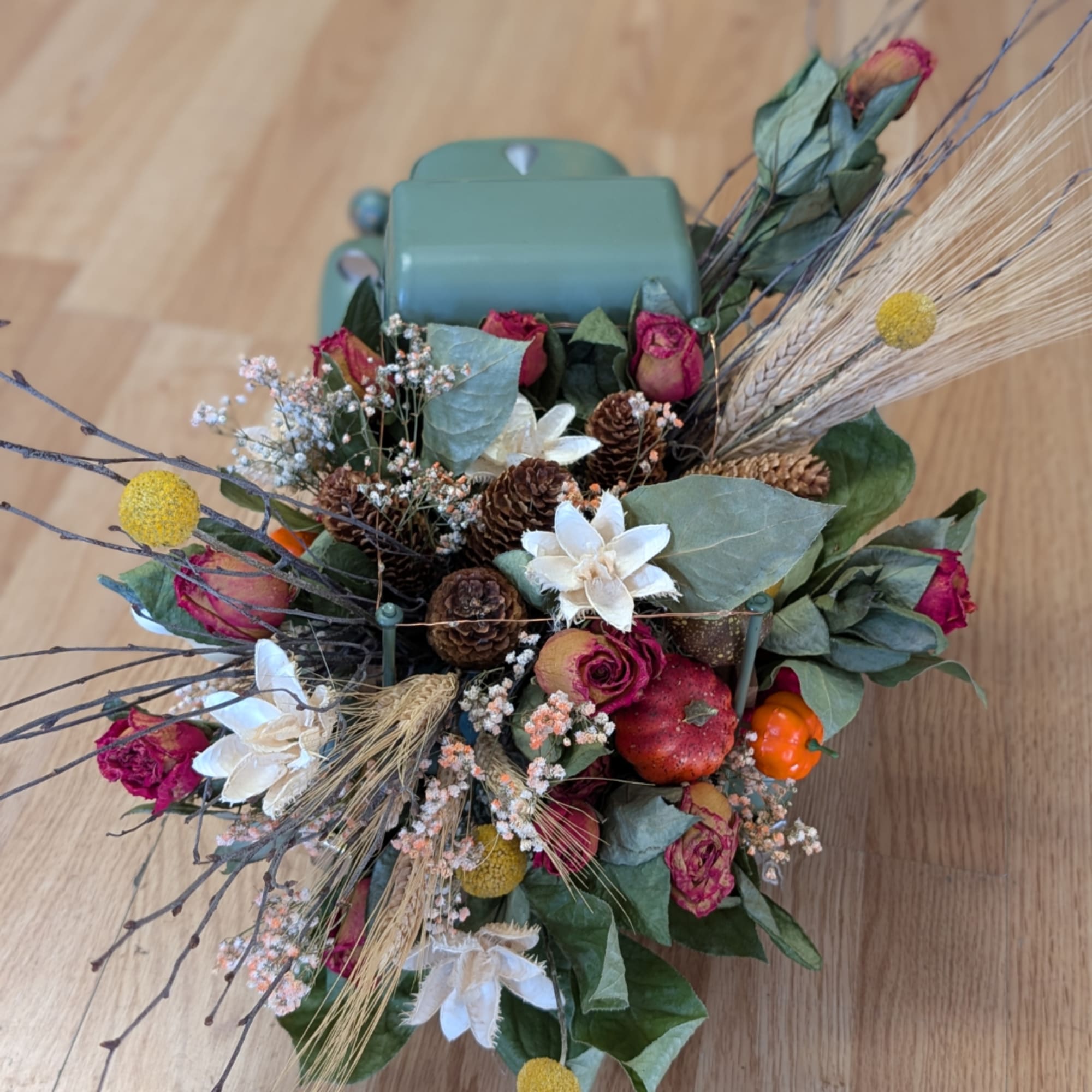 Mixed floral arrangement with roses, pinecones, and dried wheat in a teal container