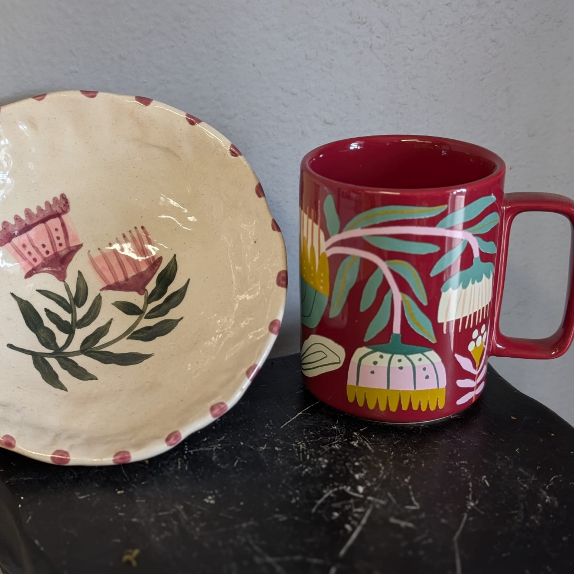 Decorative floral plate beside a red mug with painted flowers