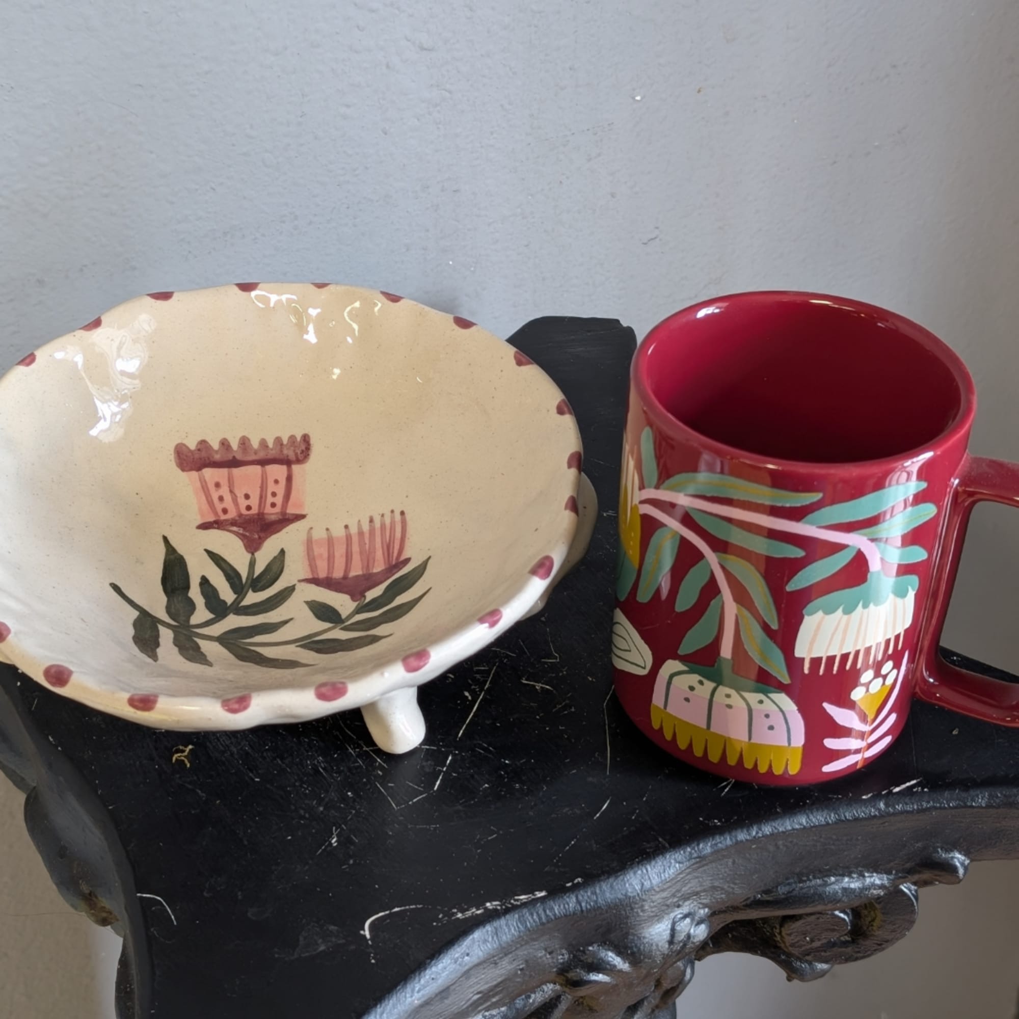 Painted ceramic bowl and red floral mug on a black stand