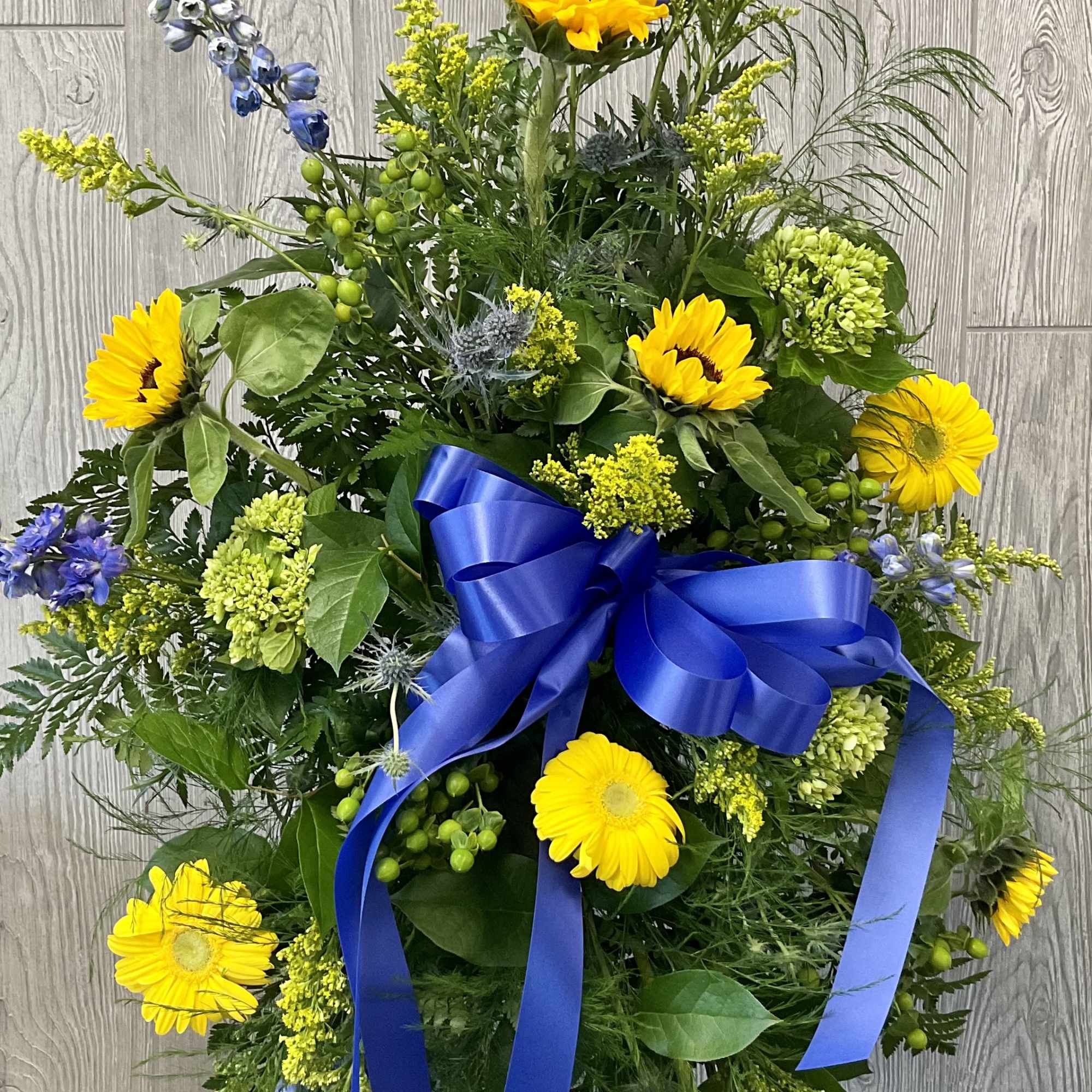 Large standing floral spray with yellow sunflowers and blue ribbon