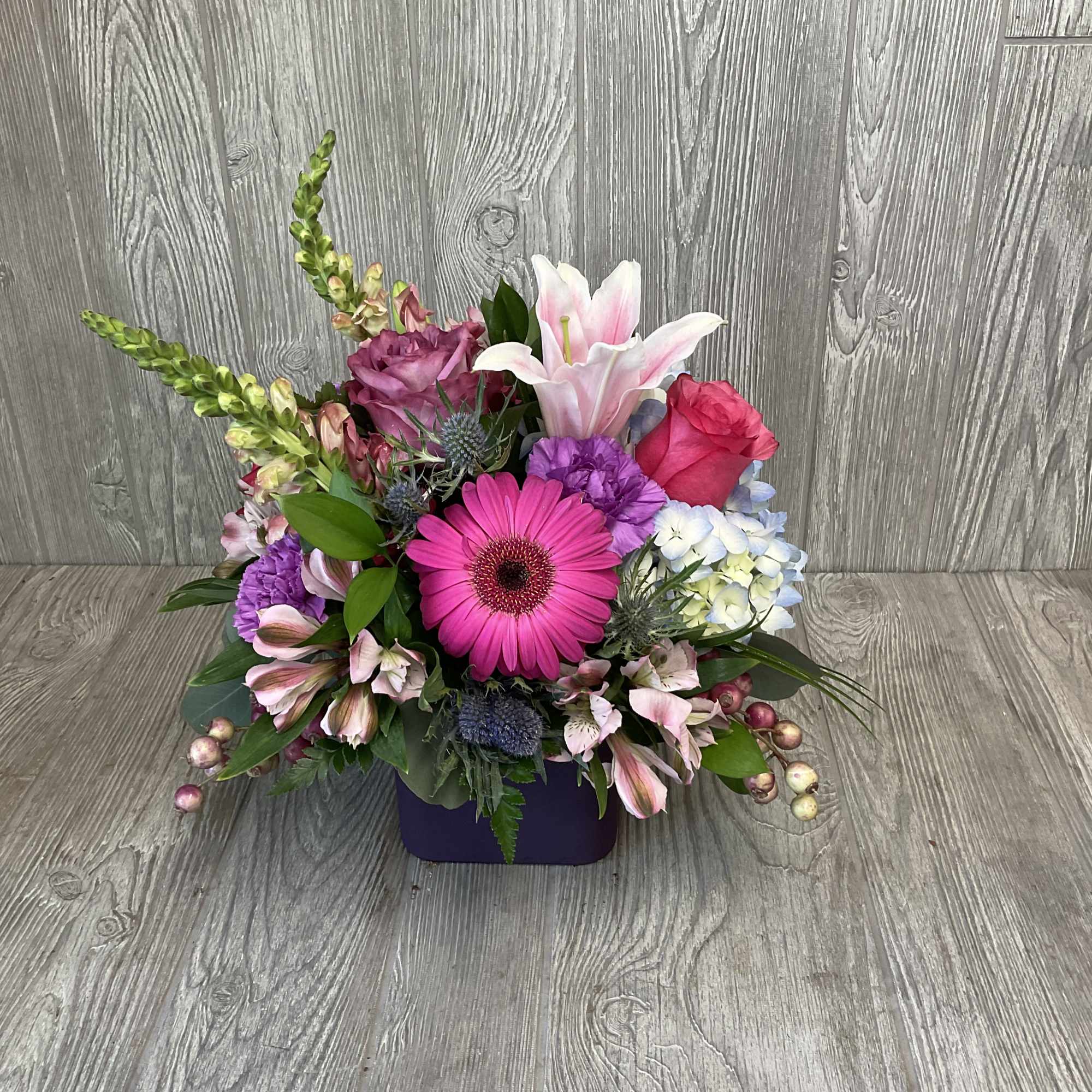 Mixed bouquet in a purple container with pink, white, and purple blooms